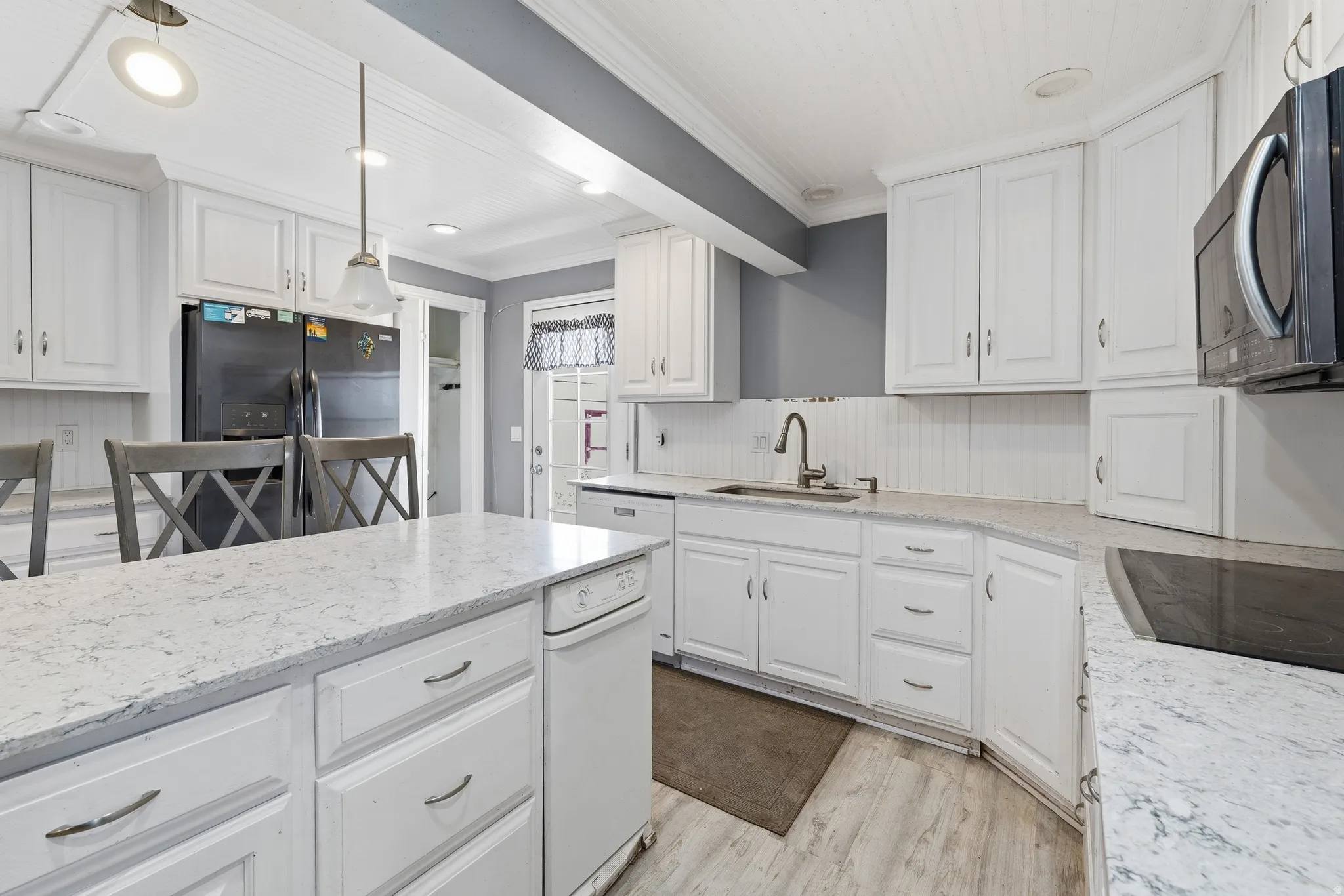 Kitchen featuring white cabinetry, light-toned countertops, integrated appliances, and wood-finish flooring