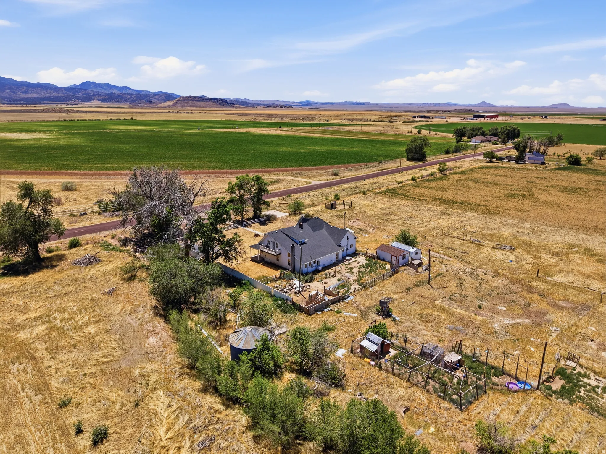 Expansive rural property featuring a white residence with a dark roof, multiple mature trees, and outbuildings