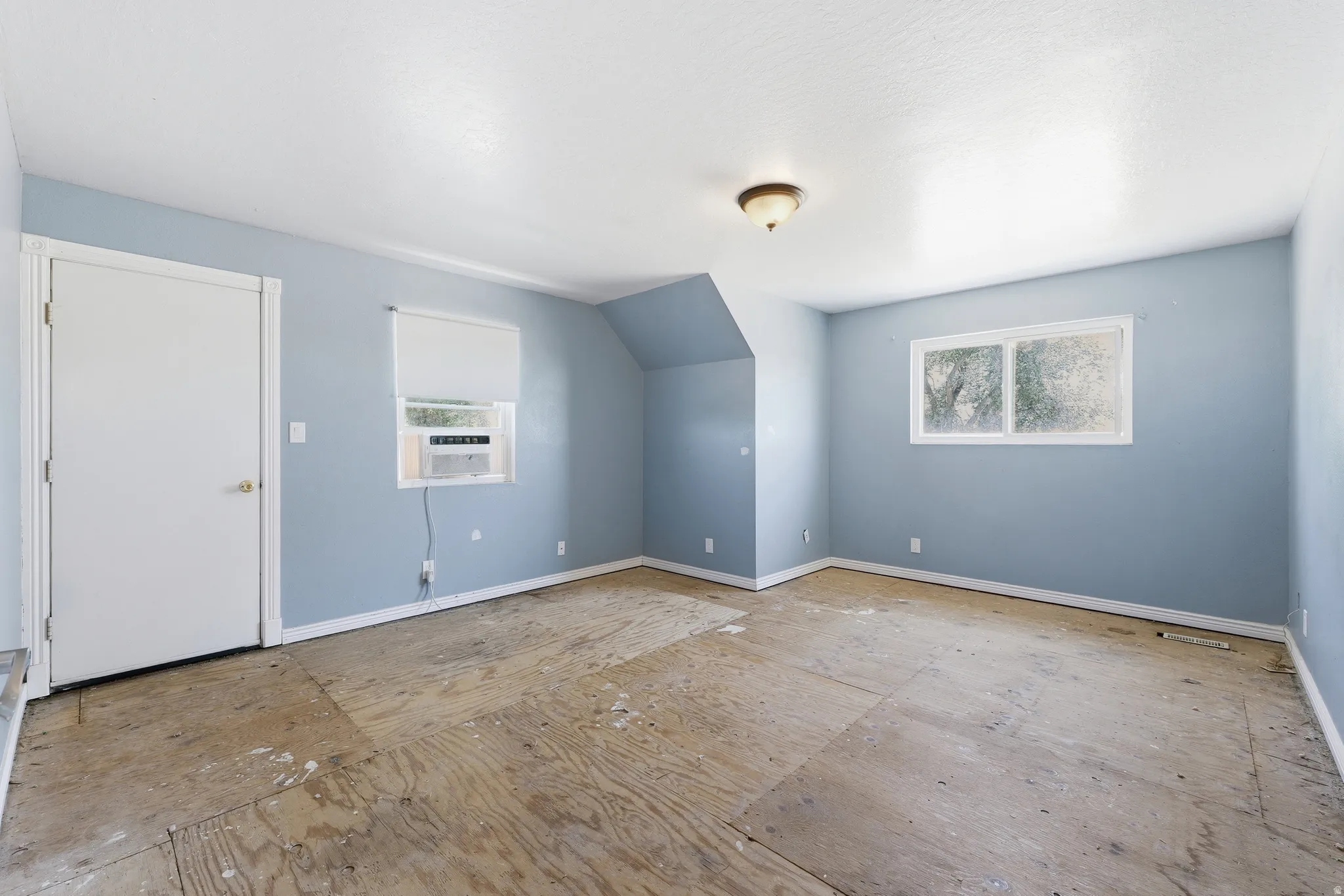 Interior room featuring light blue walls, white trim, exposed subfloor, a window air conditioning unit, and a ceiling-mounted light fixture