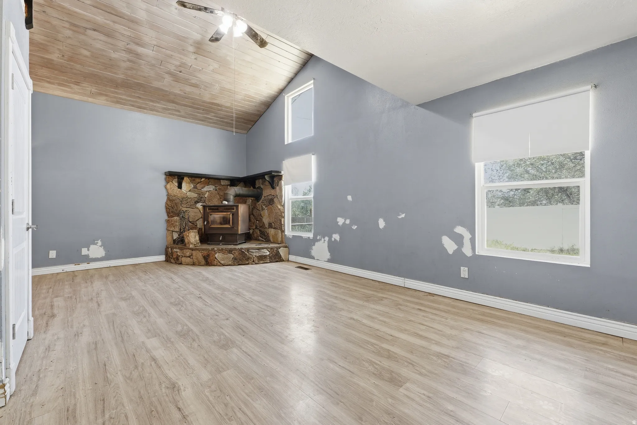 Spacious room featuring a stone-clad fireplace, vaulted wood-plank ceiling, and wood-finish flooring