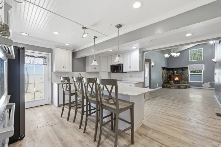 Kitchen featuring white shaker cabinetry, an island with seating, pendant lighting, beadboard ceiling, and light wood-finish flooring