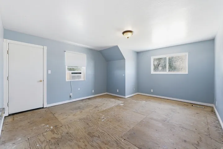 Interior room featuring light blue walls, white trim, exposed subfloor, a window air conditioning unit, and a ceiling-mounted light fixture