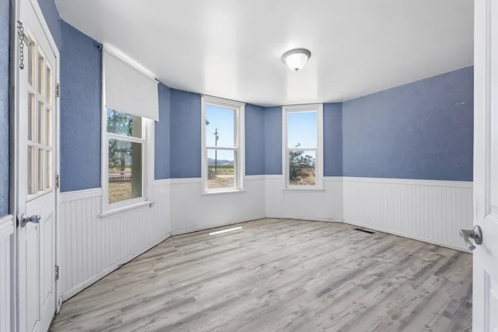 Spacious room featuring wood-finish flooring, white beadboard wainscoting, and multiple windows
