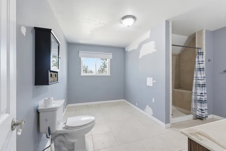 Full bathroom featuring a walk-in shower with tiled surround and built-in bench, a window with a roller shade, tile flooring, and a wall-mounted storage cabinet