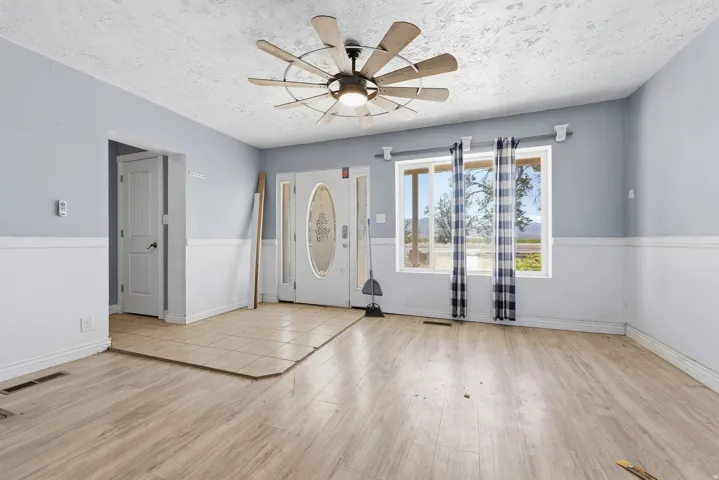 Entry foyer and living area featuring wood-finish flooring, two-tone painted walls, and a multi-blade ceiling fan with integrated lighting