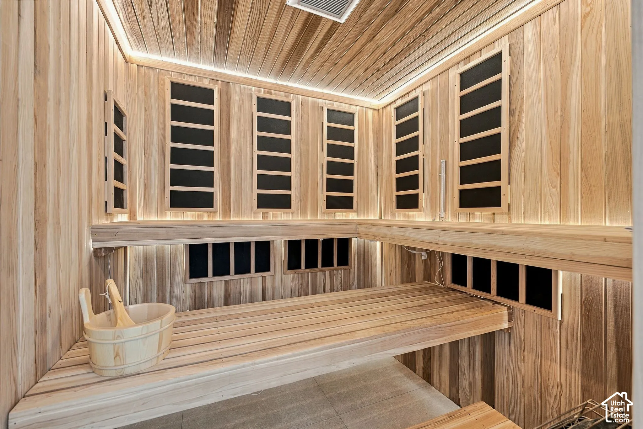 Custom sauna featuring natural wood-paneled walls and ceiling, tiered built-in wooden benches, integrated linear cove lighting, and multiple heating panels