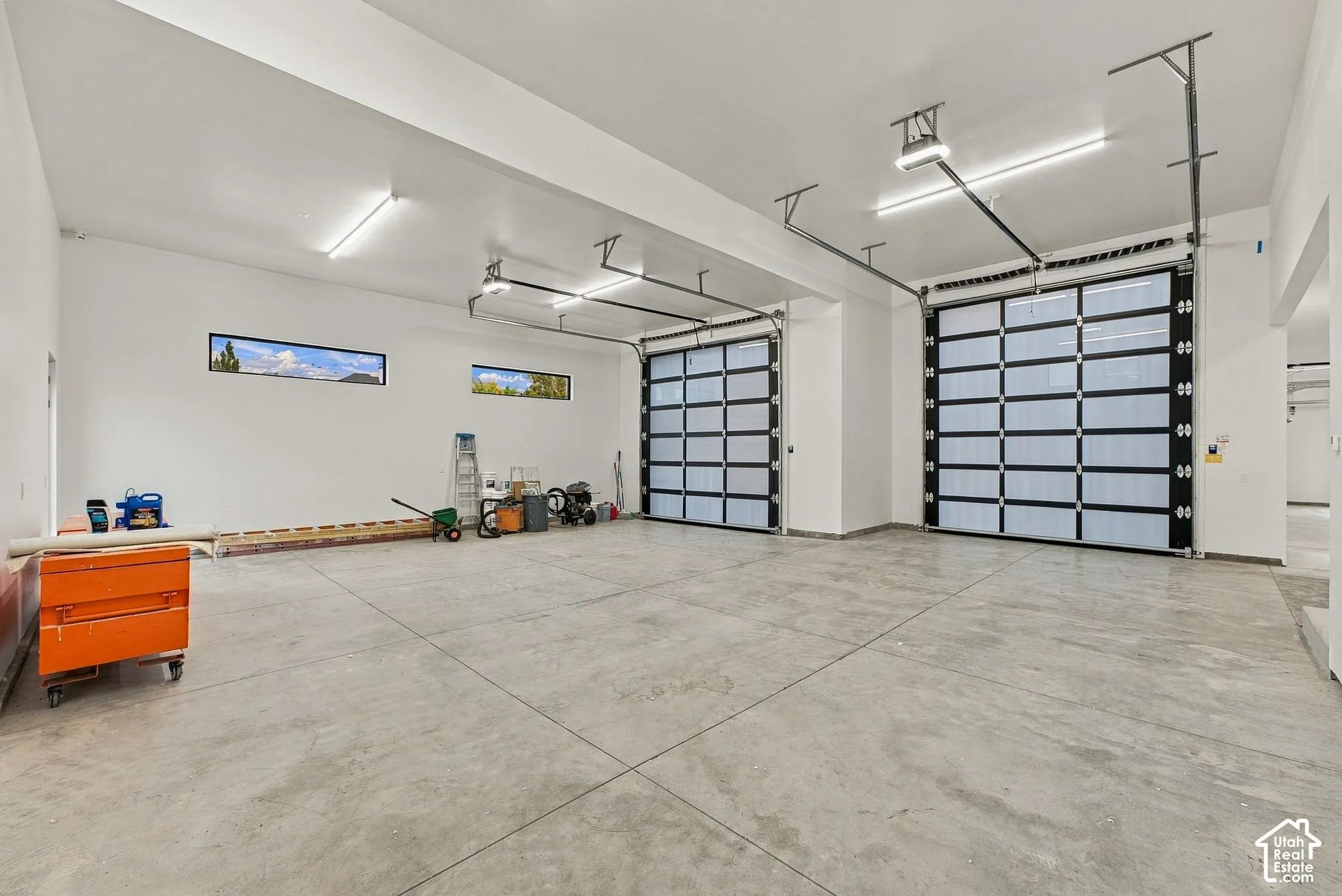 Multi-car garage featuring polished concrete flooring, high ceilings, linear LED lighting, and glass-paneled sectional overhead doors