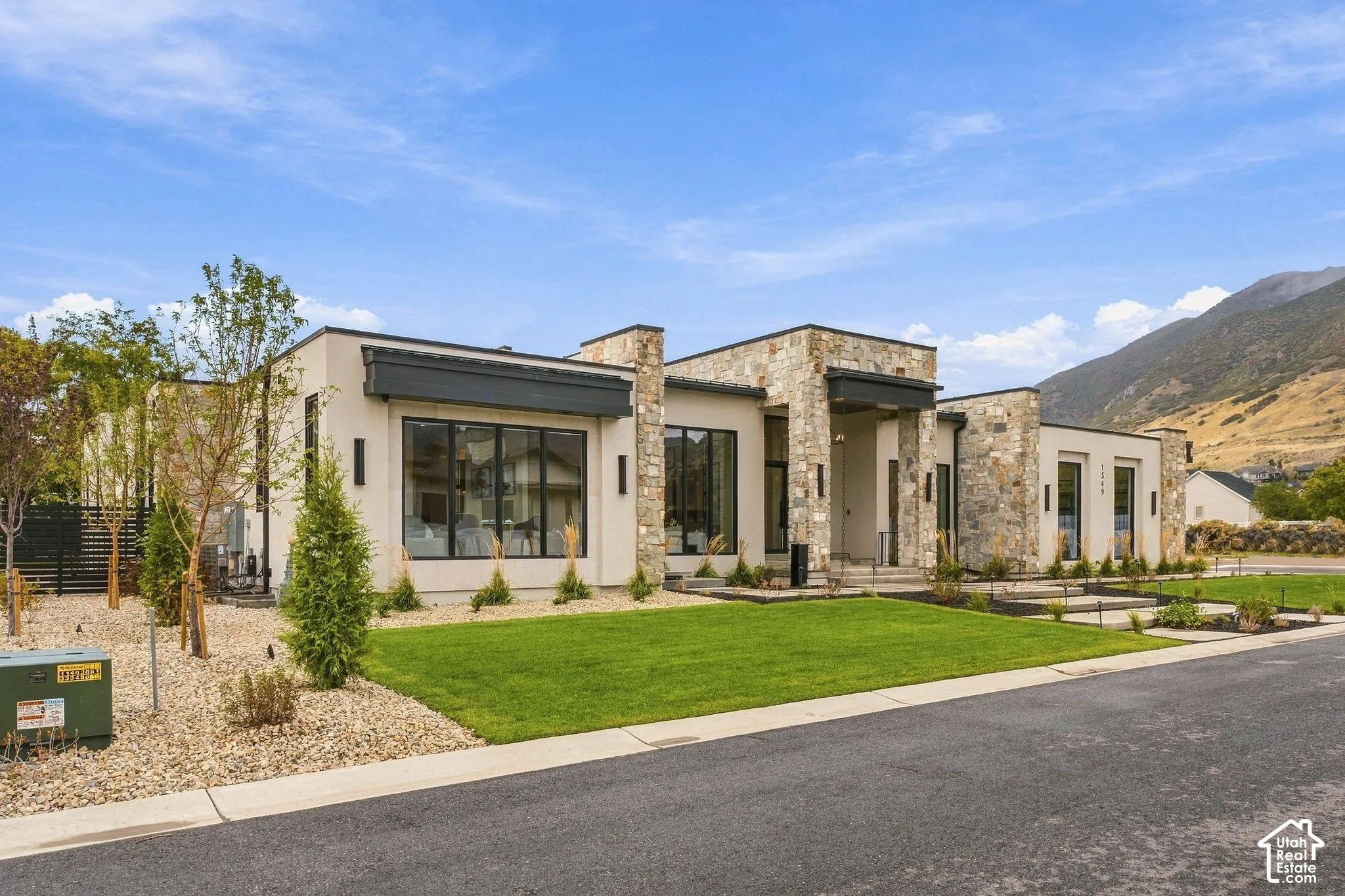 Contemporary single-story exterior featuring multi-textured stone masonry, smooth stucco siding, expansive floor-to-ceiling windows, and mountain scenery