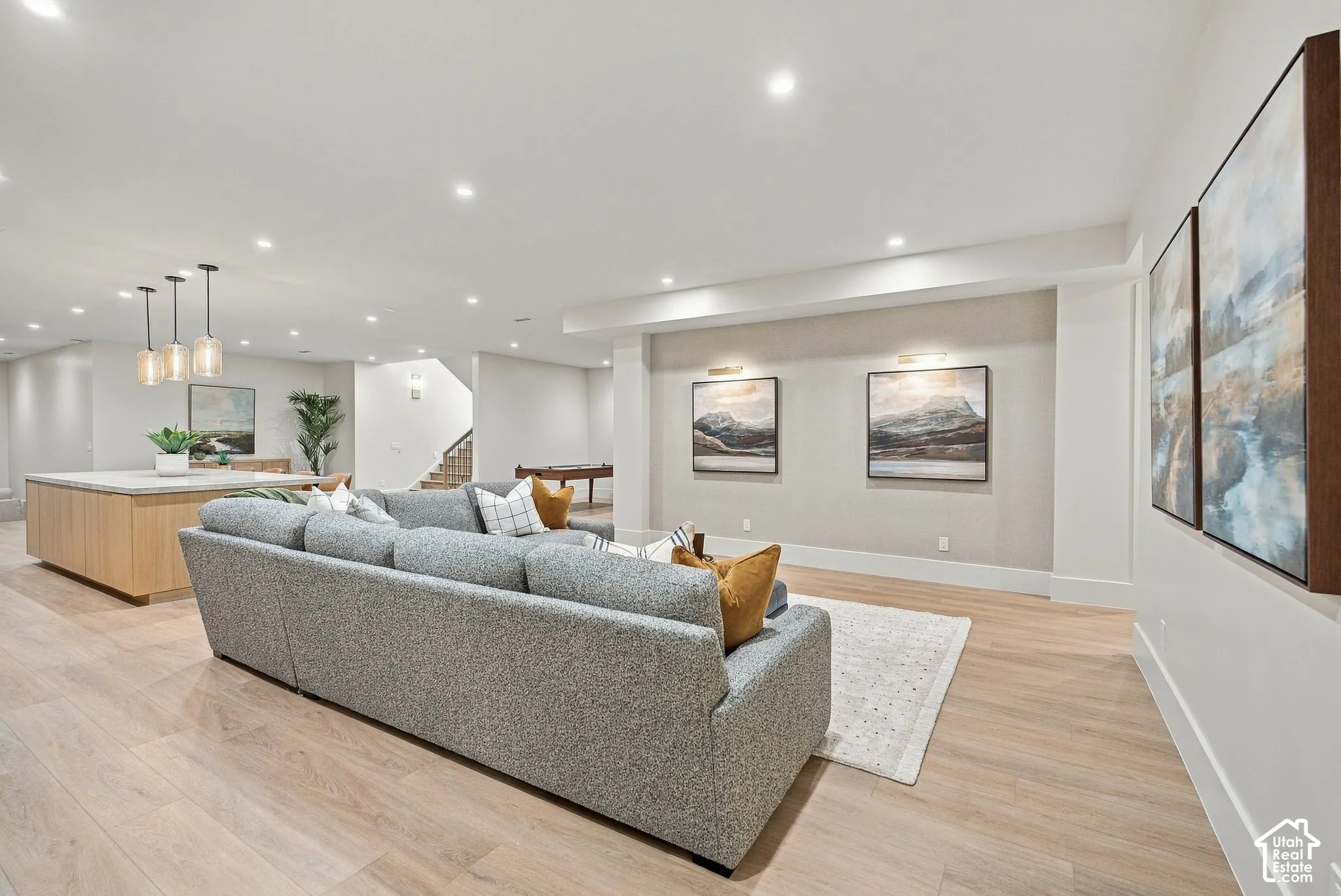 Open-concept area featuring wood-finish flooring, recessed lighting, a kitchen island with stone countertop, and wall-mounted accent lighting