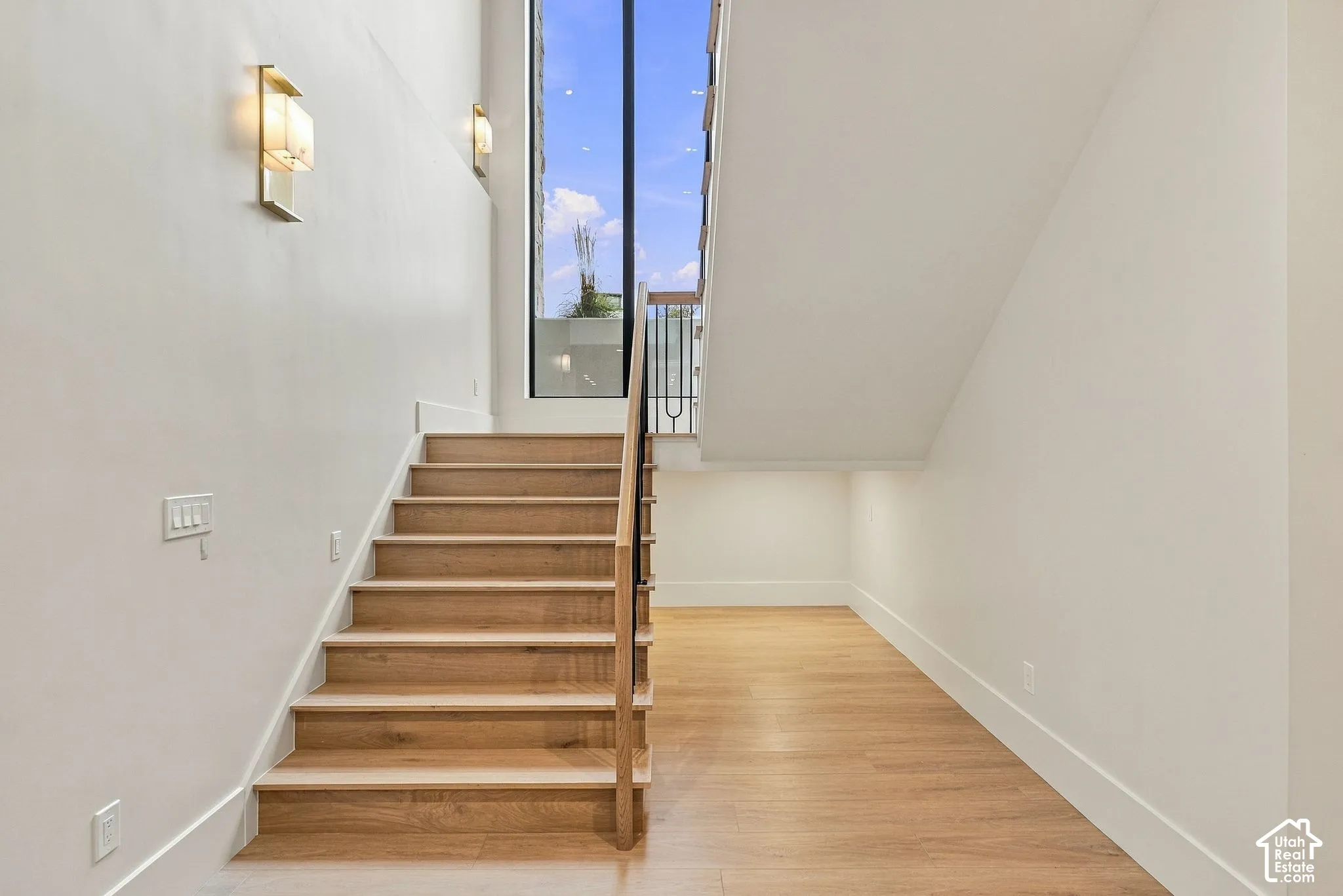 Staircase featuring wood-finish treads, a vertical floor-to-ceiling window, metal balustrades, a natural wood-finish handrail, and wall-mounted sconce lighting