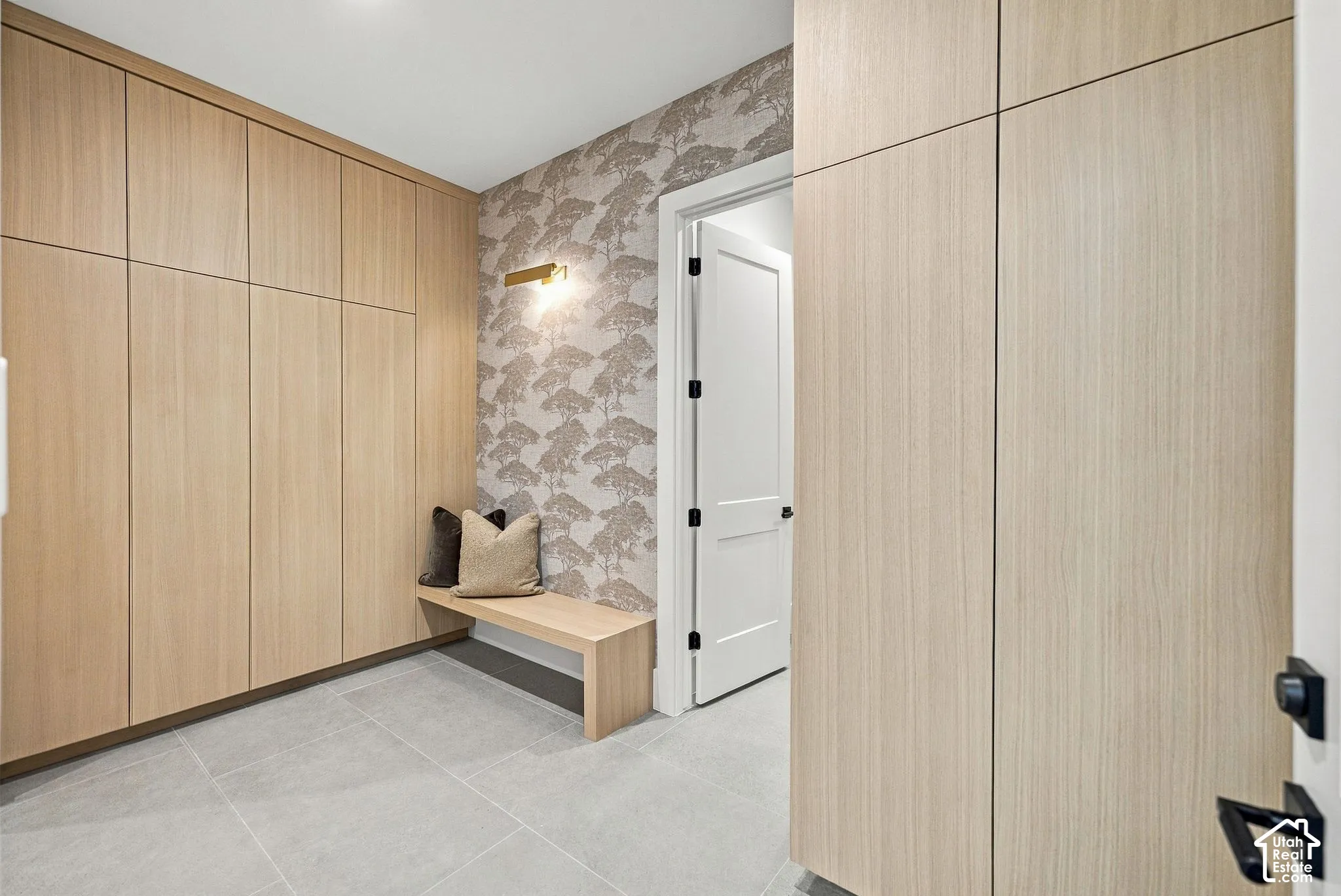 Floor-to-ceiling wood-finish cabinetry, tile flooring, integrated wood-finish bench, patterned wall covering, and wall-mounted lighting