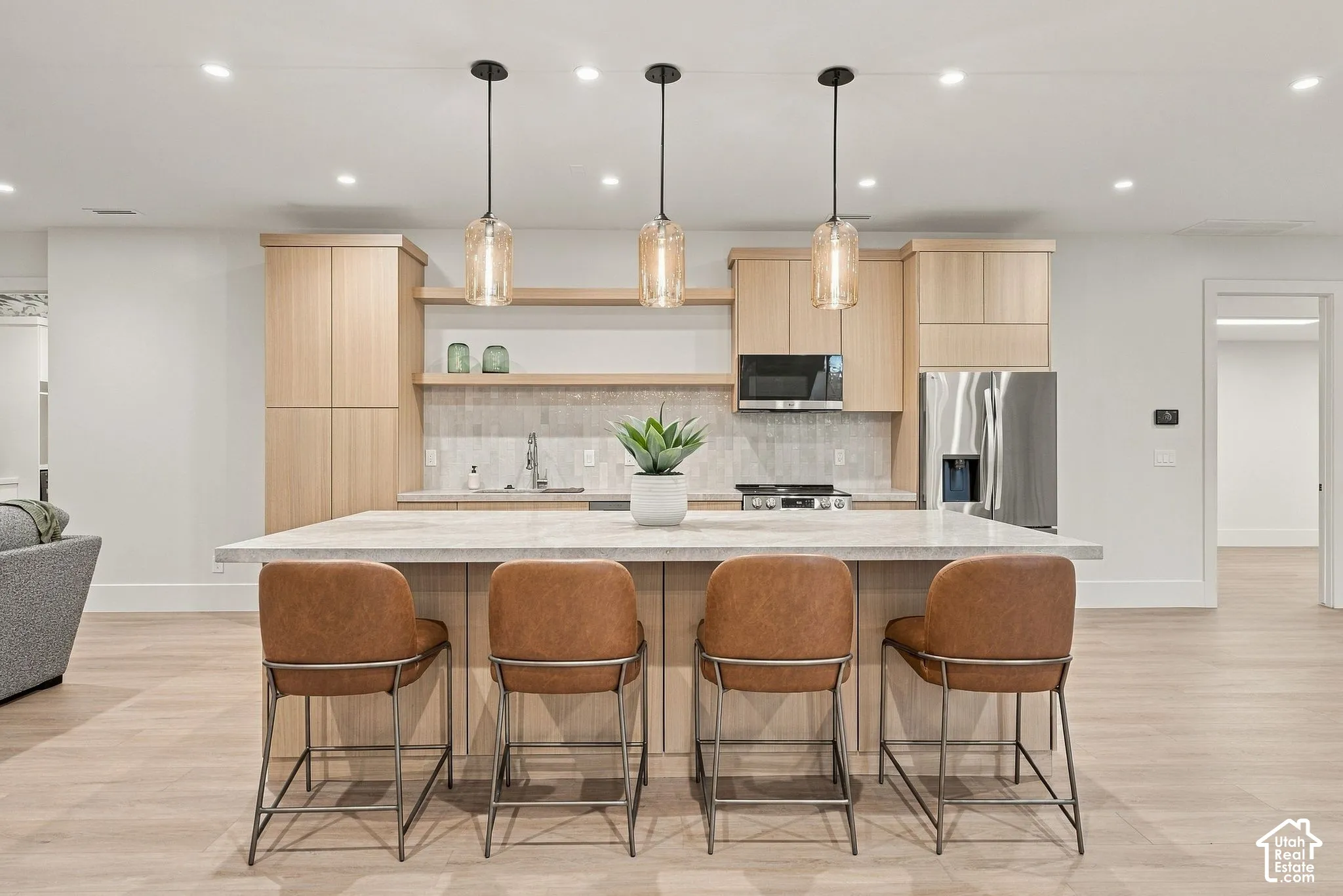 Kitchen featuring light wood-finish cabinetry, a central island with a stone-composite countertop, stainless steel appliances, recessed ceiling lighting, and glass pendant fixtures