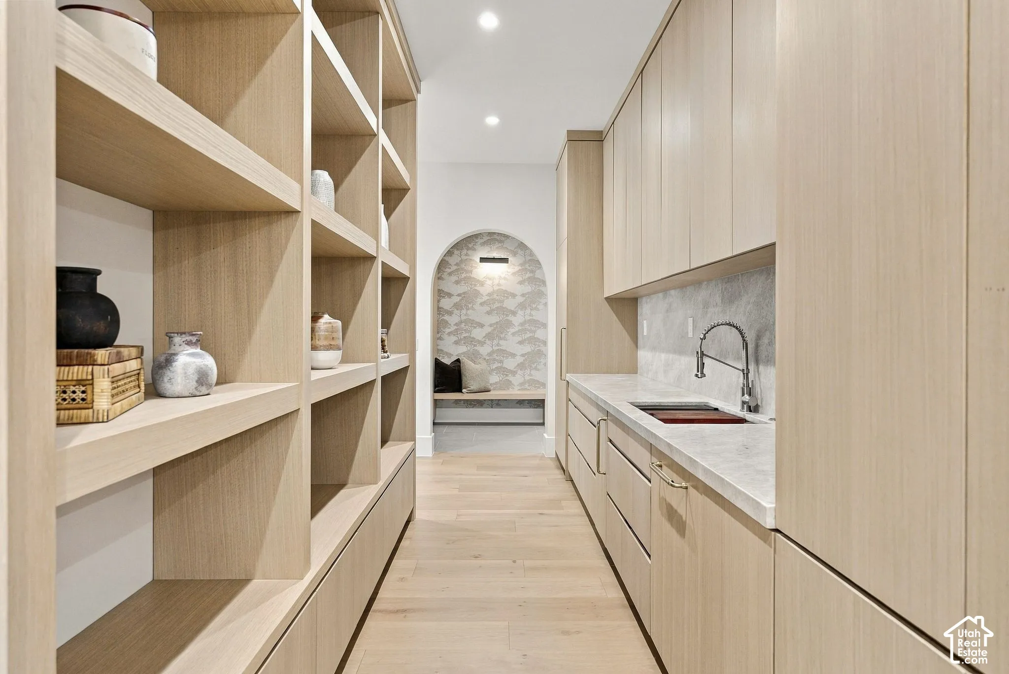 Custom light wood cabinetry, integrated stone-surface countertop with undermount sink, built-in shelving, and arched architectural feature with patterned accent wall