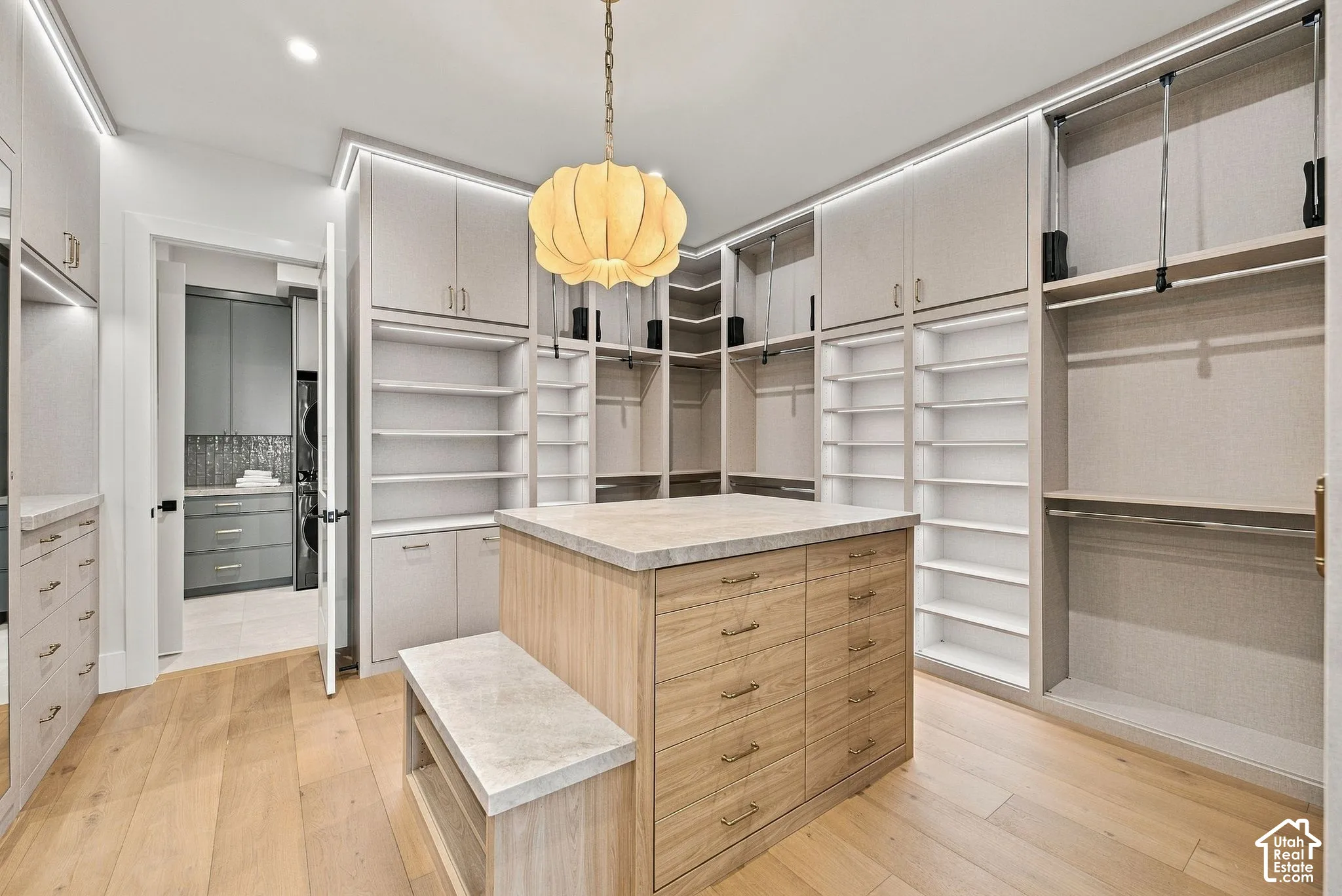 Custom walk-in closet featuring extensive built-in cabinetry, integrated LED lighting, a central island with stone countertop, and wood-finish flooring
