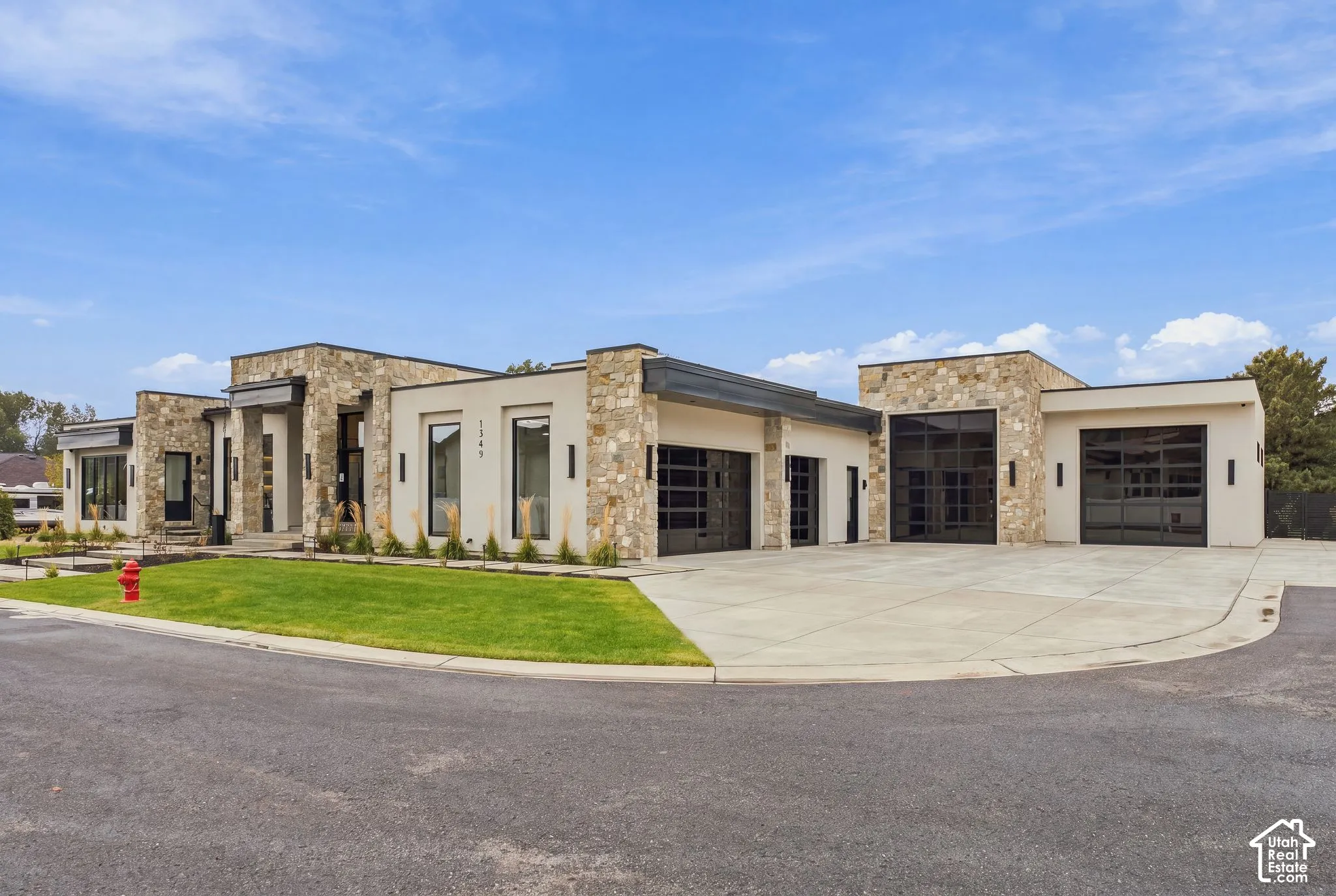 Contemporary exterior featuring stone veneer accents, smooth stucco finish, multi-car garage with glass-paneled doors, and concrete driveway
