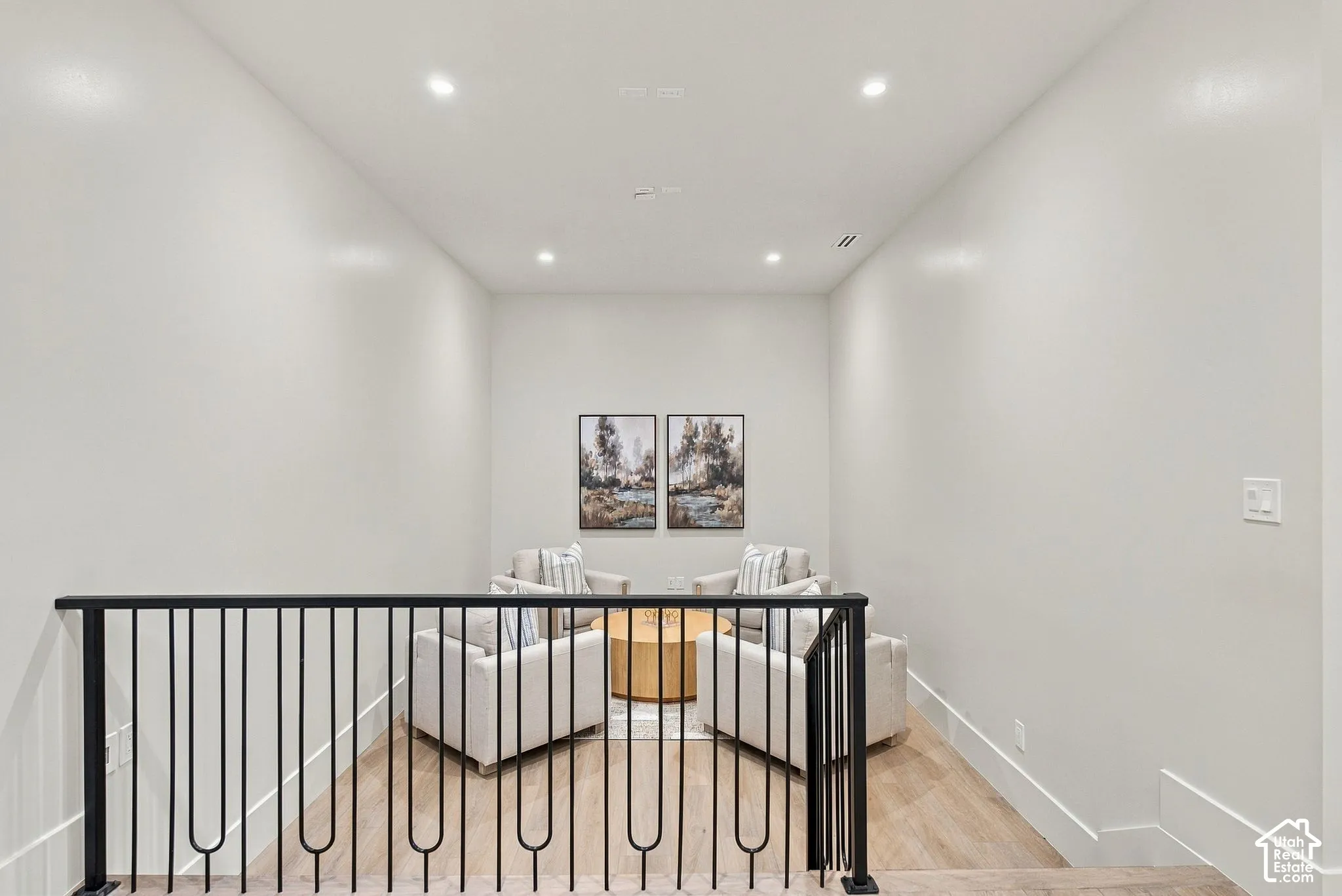 Neutral-toned interior space featuring wood-finish flooring, recessed ceiling lighting, and a metal railing with vertical balusters