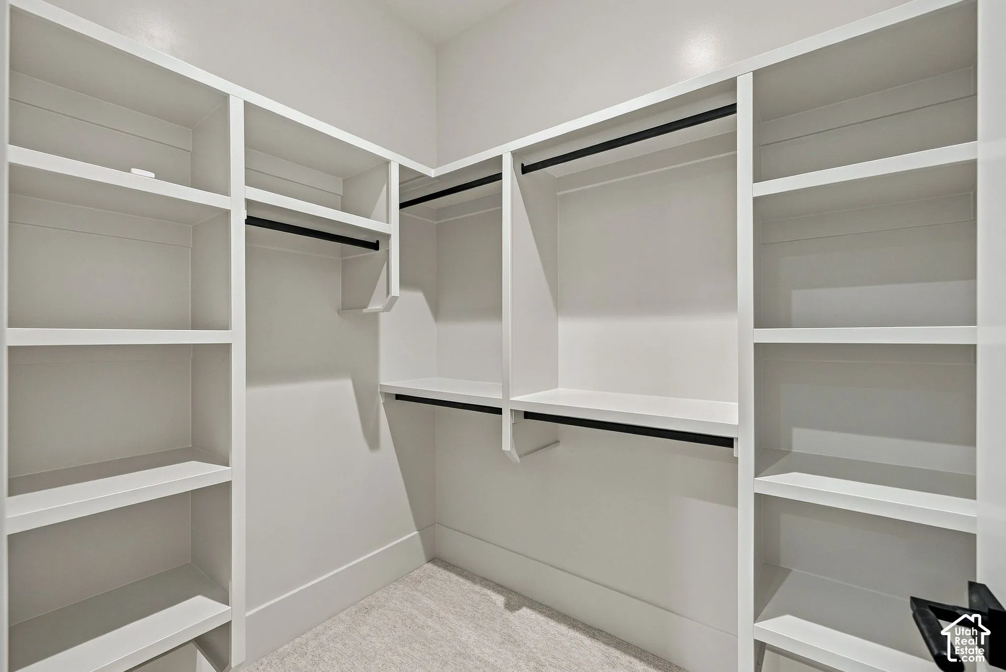 Walk-in closet featuring custom white built-in shelving, multiple hanging rods, and neutral carpeting