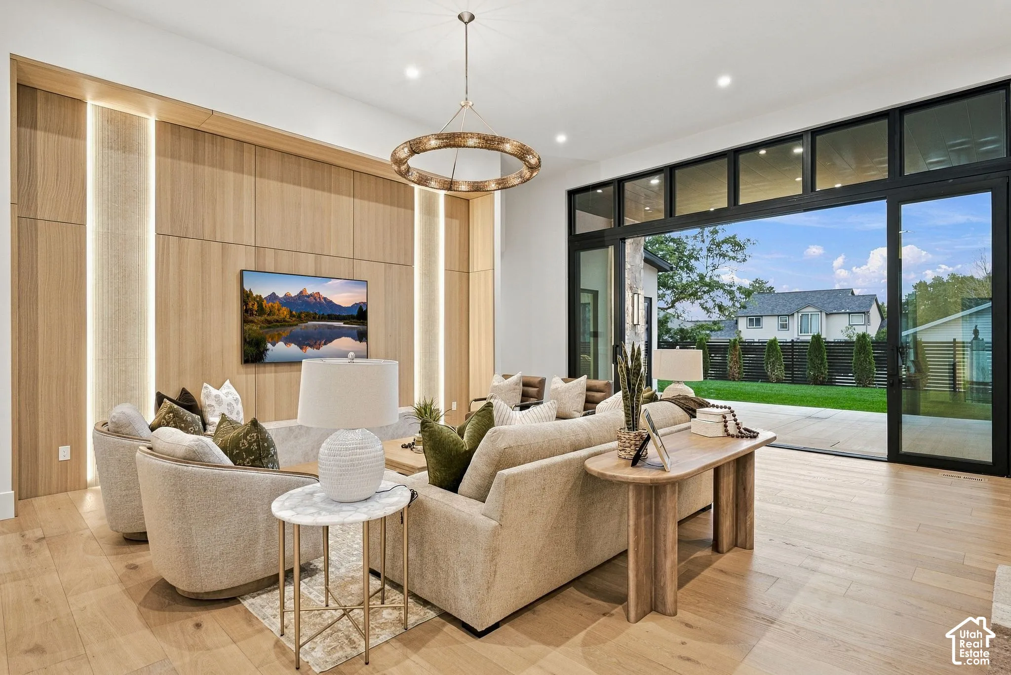 Wood-finish flooring, custom wood wall paneling with integrated vertical accent lighting, large-scale multi-panel sliding glass doors, and a circular geometric chandelier
