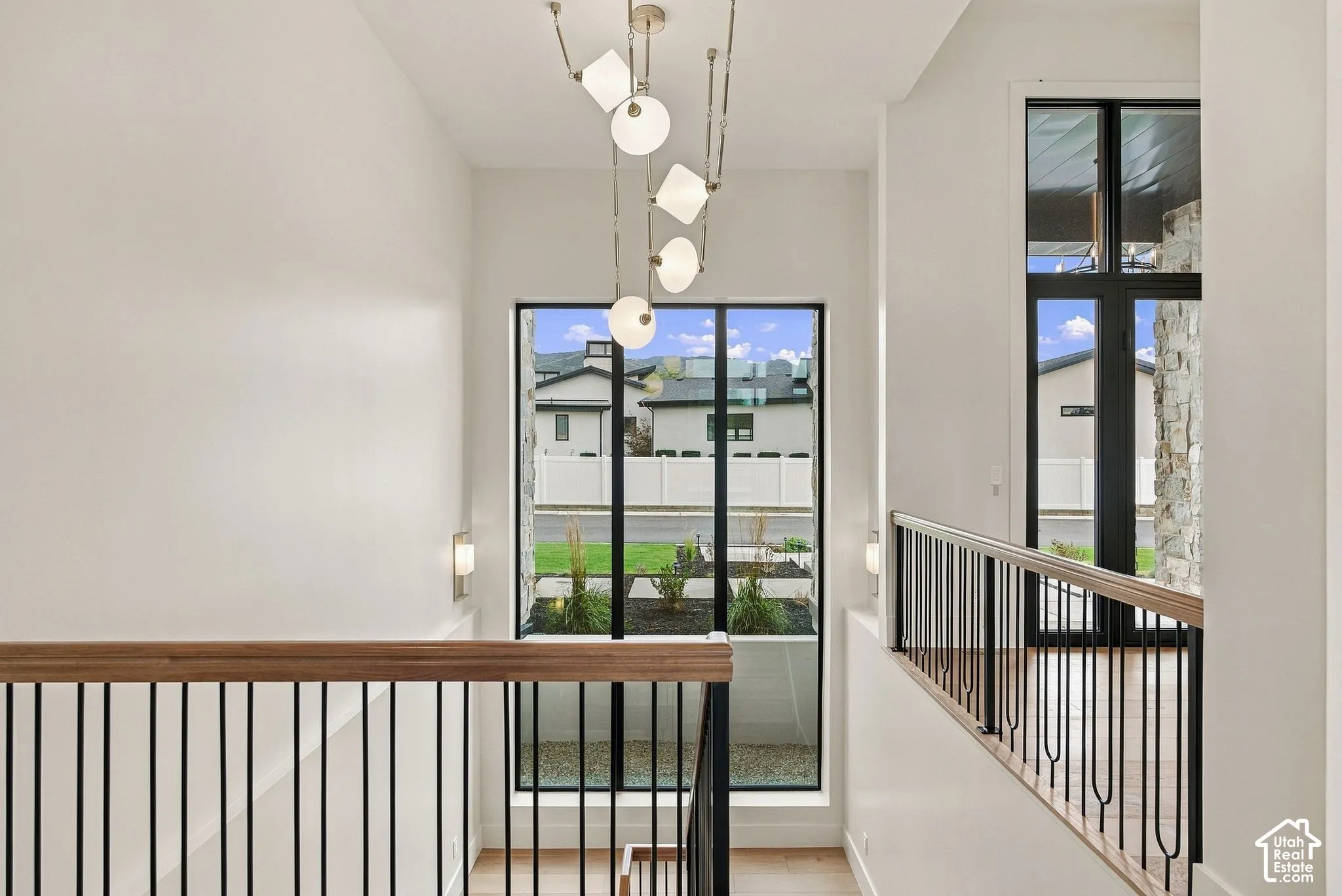 Entryway featuring a multi-globe pendant light fixture, black metal railings with wood-finish handrails, and floor-to-ceiling windows with black framing