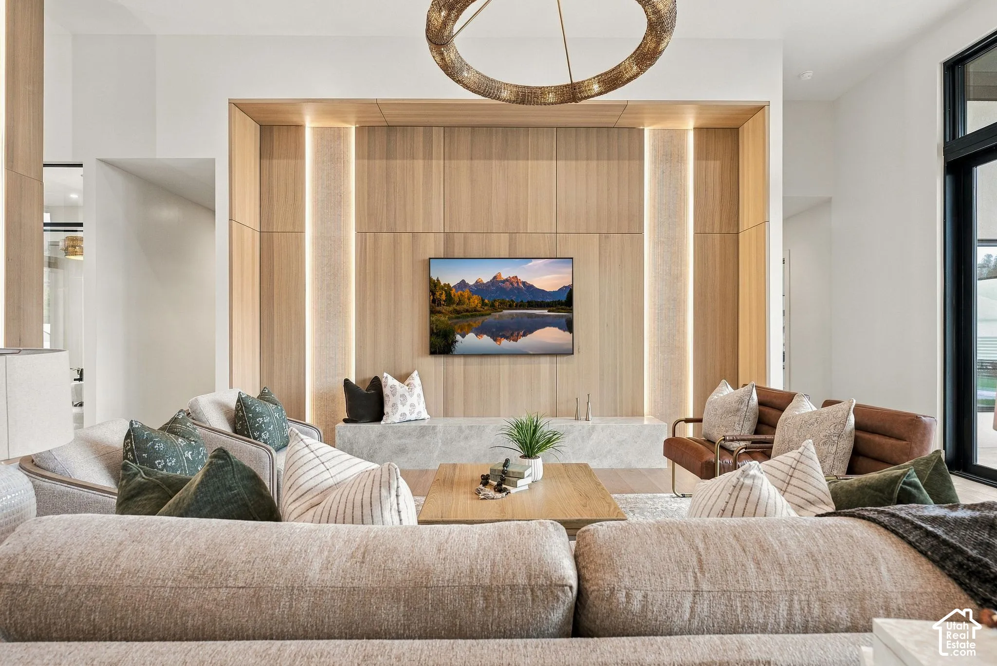 Floor-to-ceiling wood paneling with integrated vertical accent lighting, stone-top built-in media console, and circular chandelier