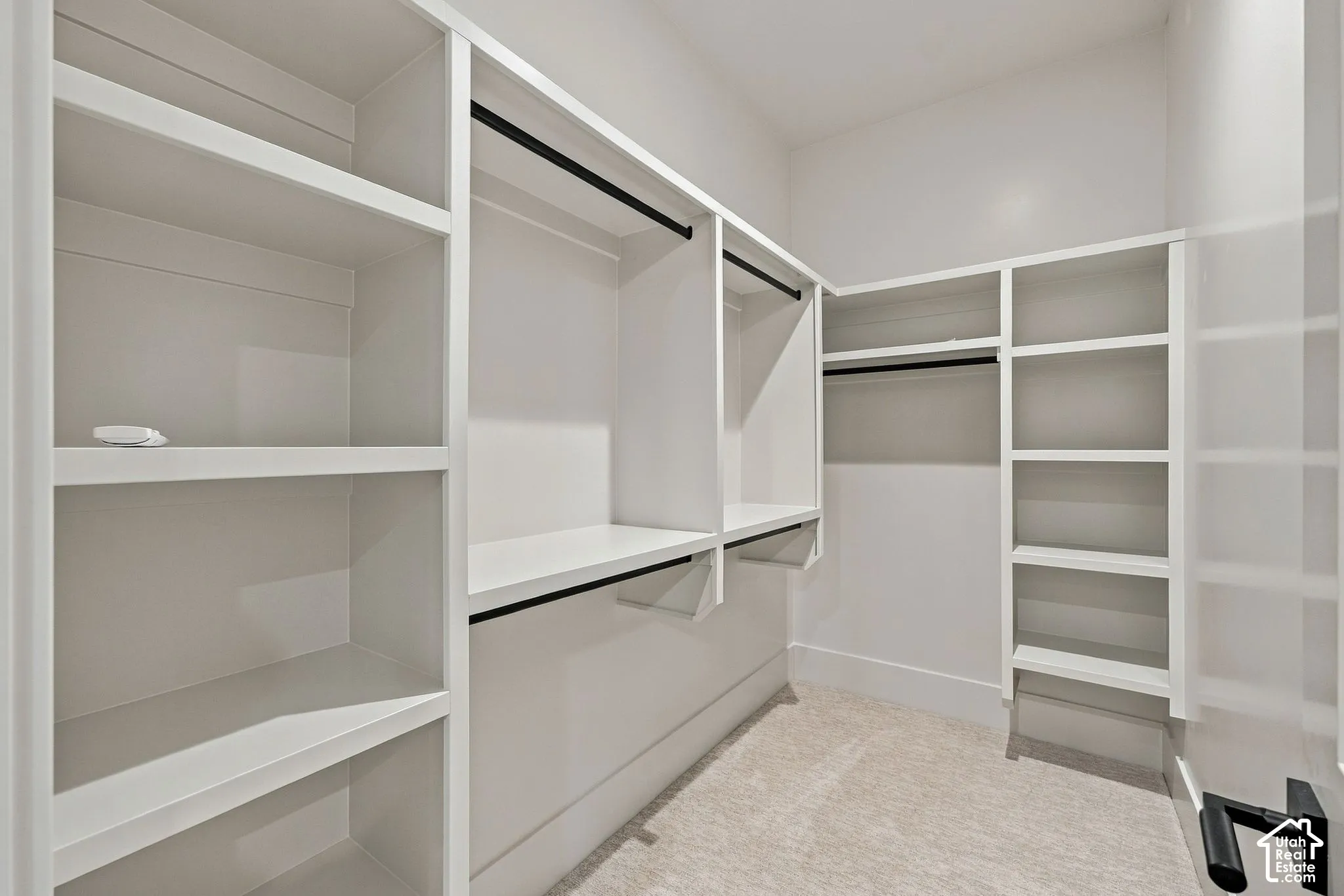 Custom walk-in closet featuring white built-in shelving, hanging rods, and neutral carpeting