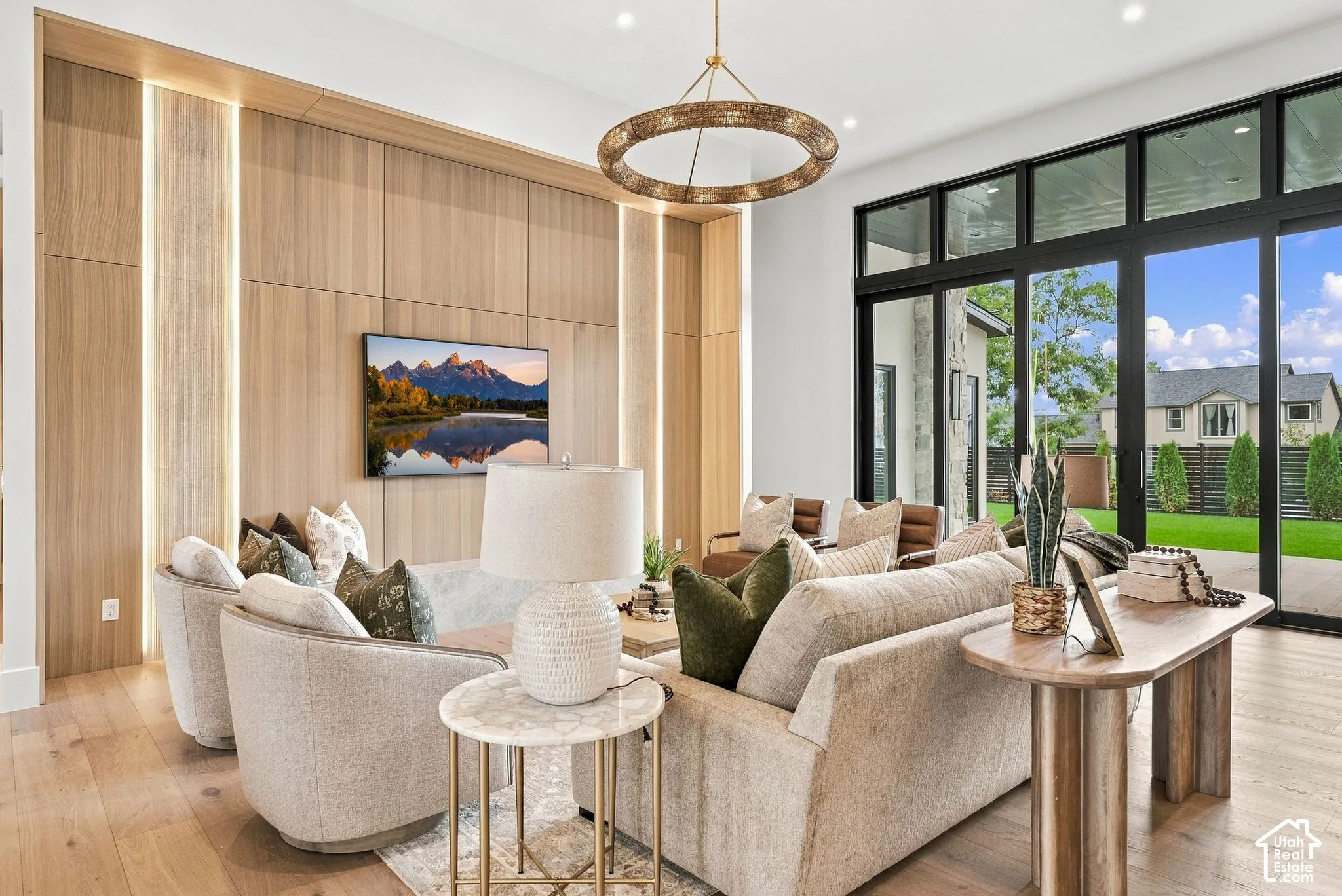 Floor-to-ceiling white oak wood paneling and stone with integrated vertical ambient accent lighting, light-toned wood-finish flooring, recessed ceiling lighting, and large-format multi-panel glass doors