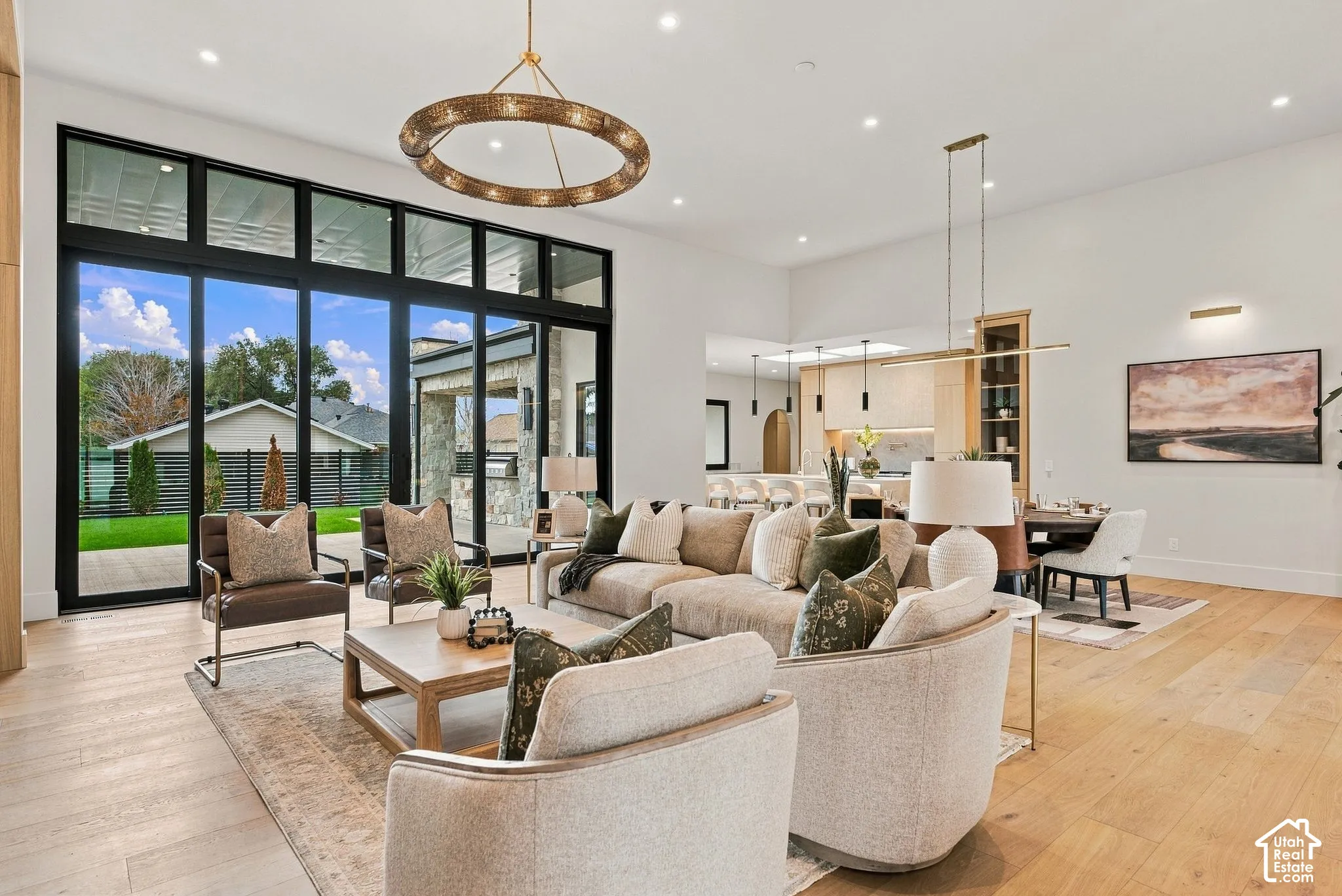 Open-concept living space featuring wood-finish flooring, floor-to-ceiling black-frame multi-panel glass doors, a large circular chandelier, and recessed lighting