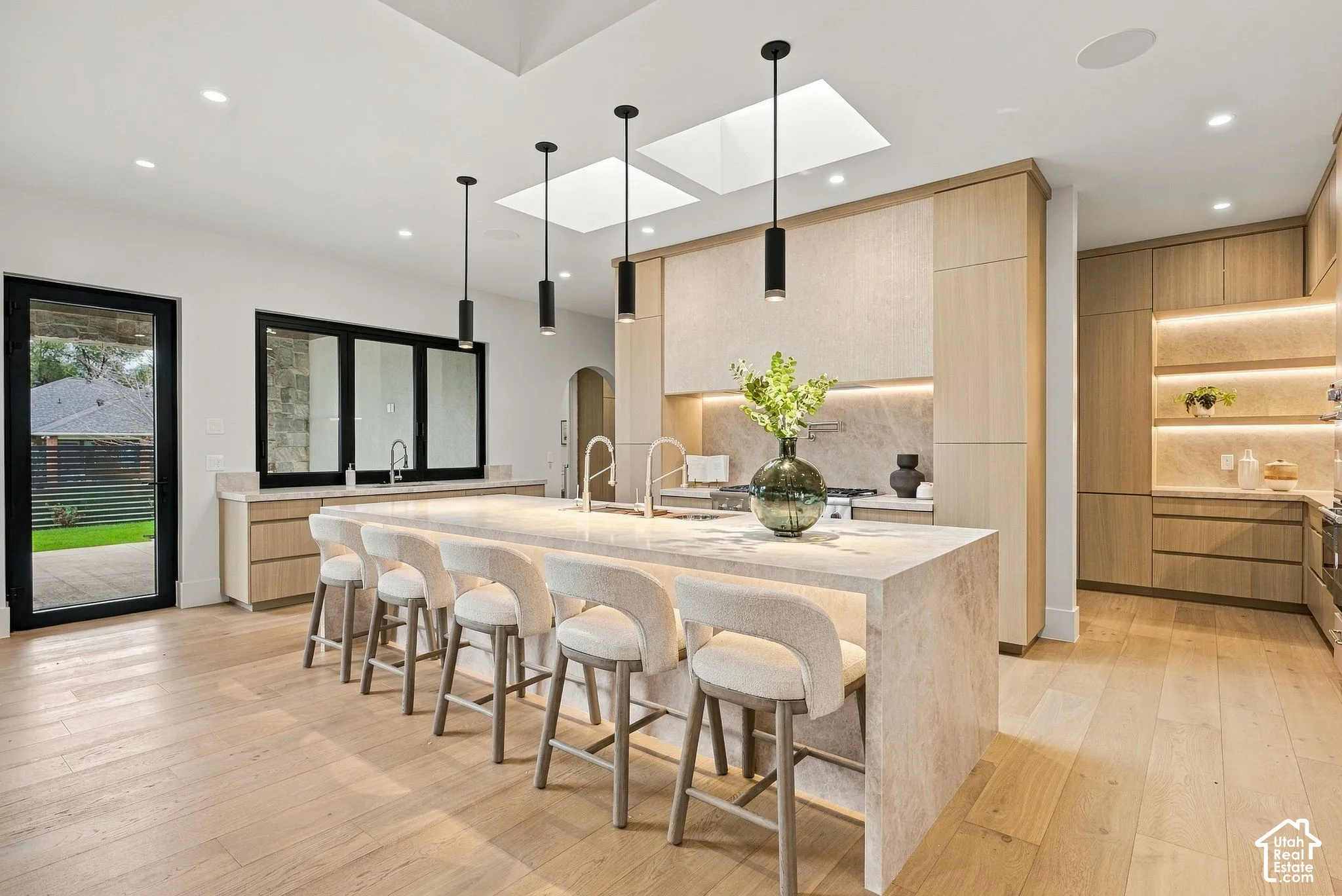 Kitchen featuring a waterfall-edge Taj Mahal stone island, white oak cabinetry, two ceiling skylights for optimum natural light,  pendant lighting, and hardwood flooring. Thermador appliances, 6 ft refrigerator, 3 dishwashers, workstation sinks, custom st