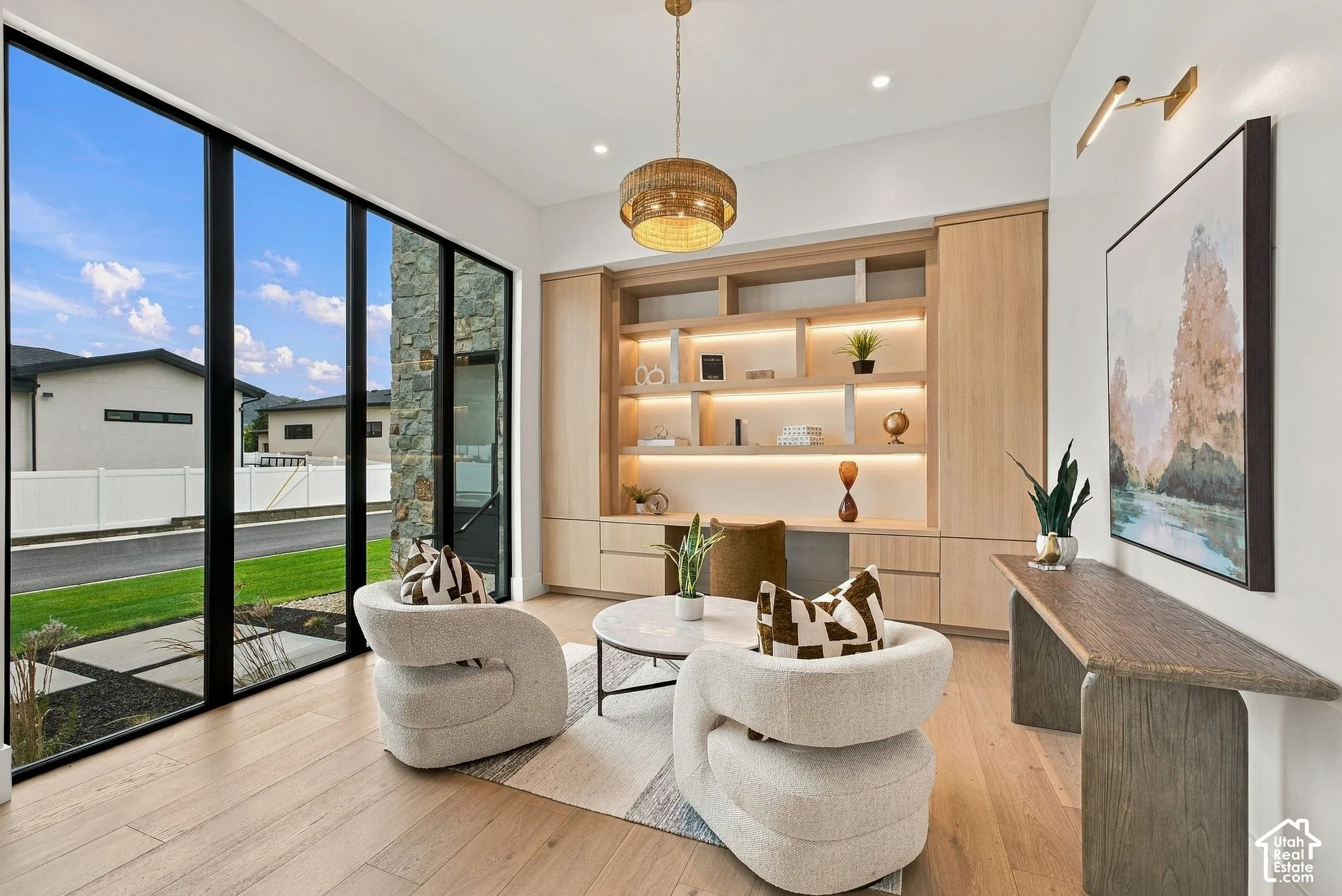 Floor-to-ceiling windows, custom built-in white oak cabinetry with integrated lighting, wood-finish flooring, and a textured drum pendant light