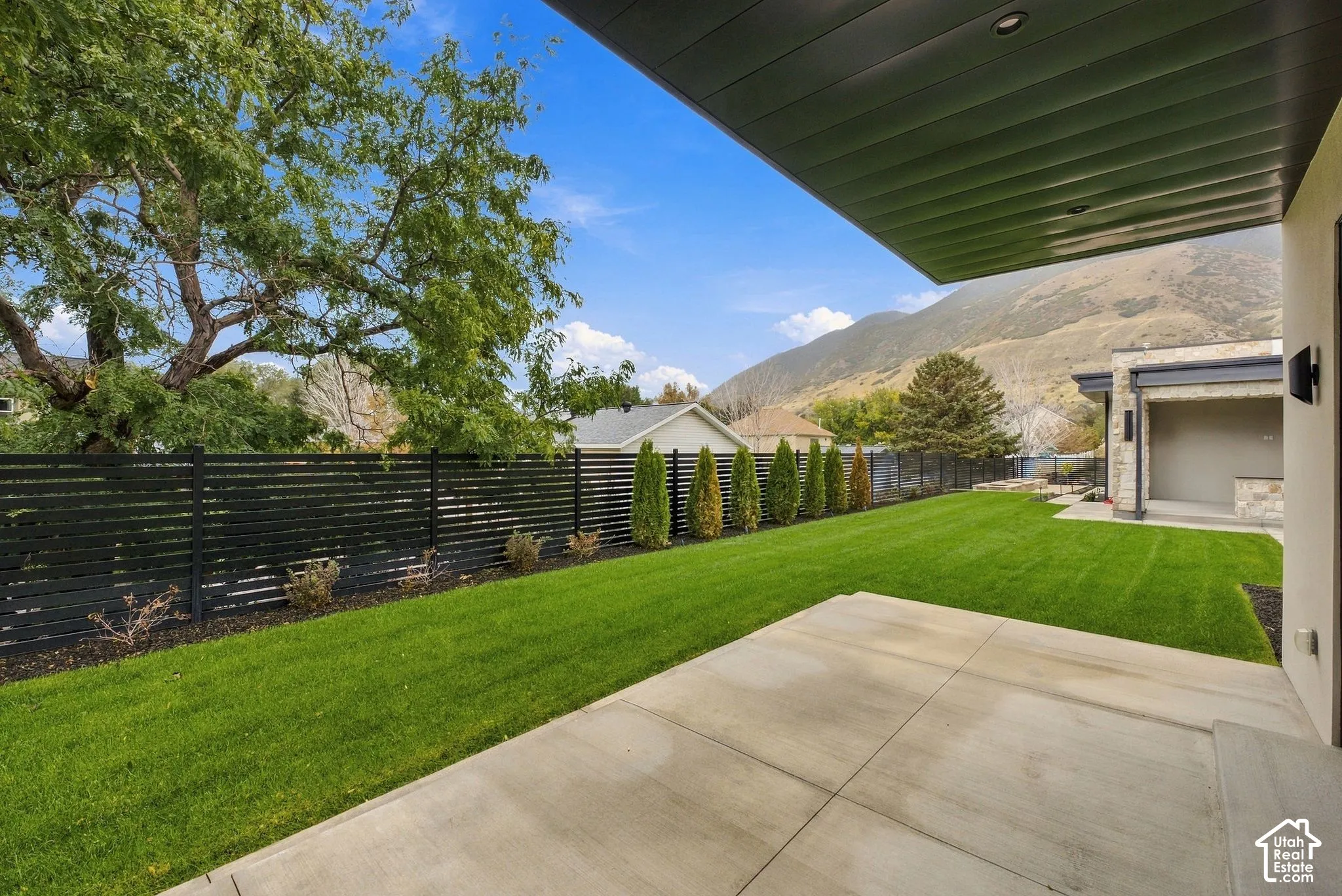 Covered concrete patio featuring a horizontal slat privacy fence, manicured lawn, and mountain backdrop