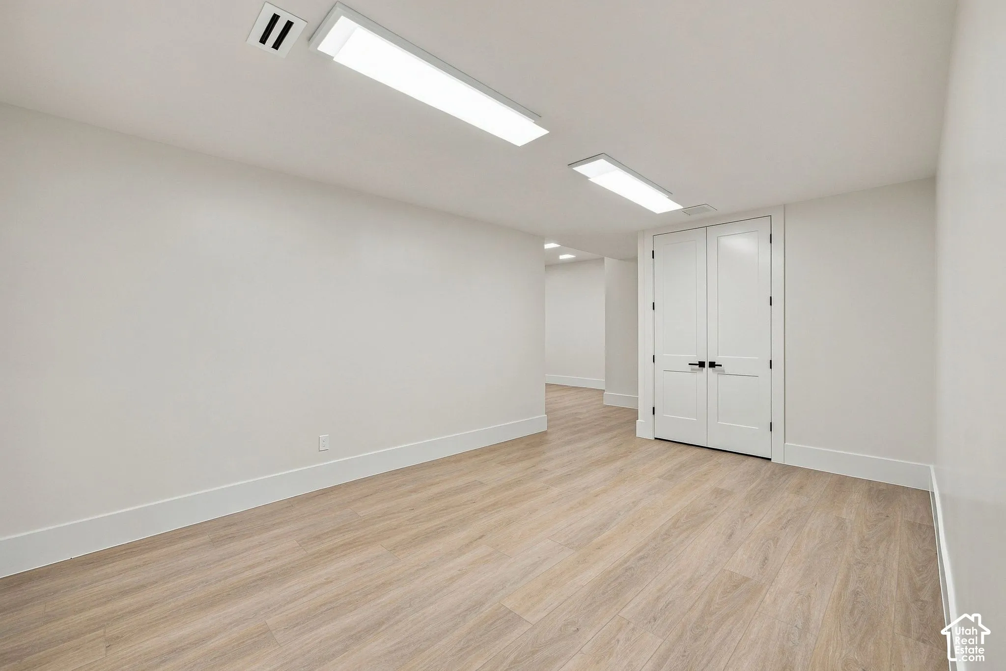 Interior space featuring wood-finish flooring, dual panel doors with matte black hardware, and linear ceiling-mounted lighting