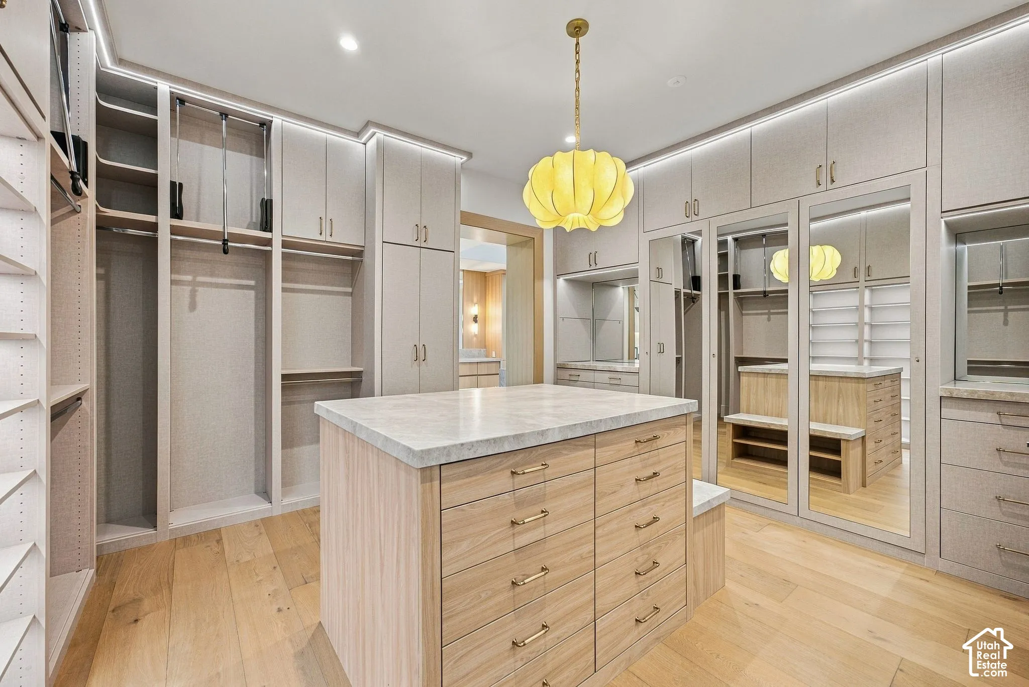 Custom closet featuring floor-to-ceiling cabinetry, integrated lighting, wood-finish flooring, a central storage island with a stone-top surface, and full-length mirrored doors