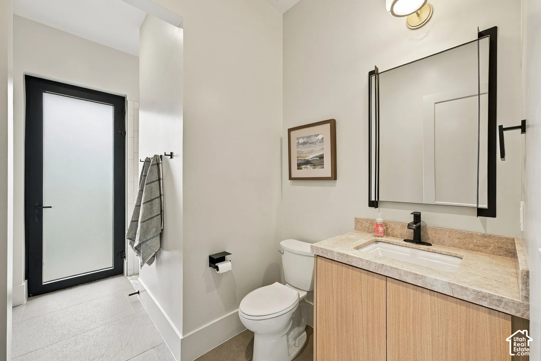 Bathroom off of mudroom with a shower for future pool use, Light-toned wood vanity with a stone countertop, rectangular undermount sink, matte black faucet, and rectangular mirror with a metal frame