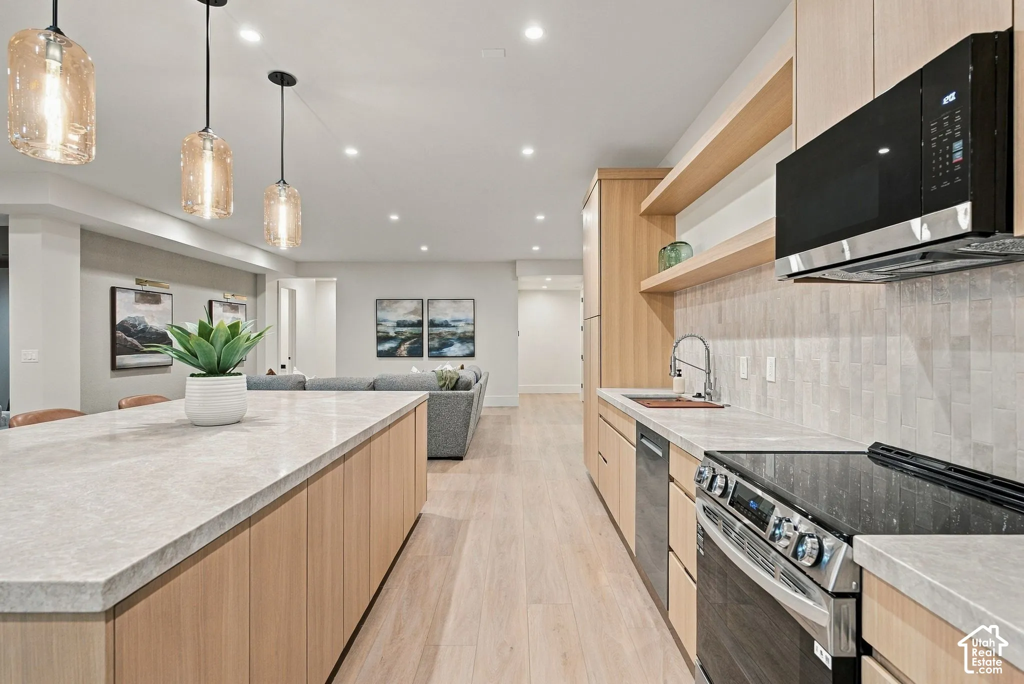 Kitchen featuring light wood-finish cabinetry, stone-surface countertops, textured tile backsplash, floating wood shelving, and three glass pendant lights