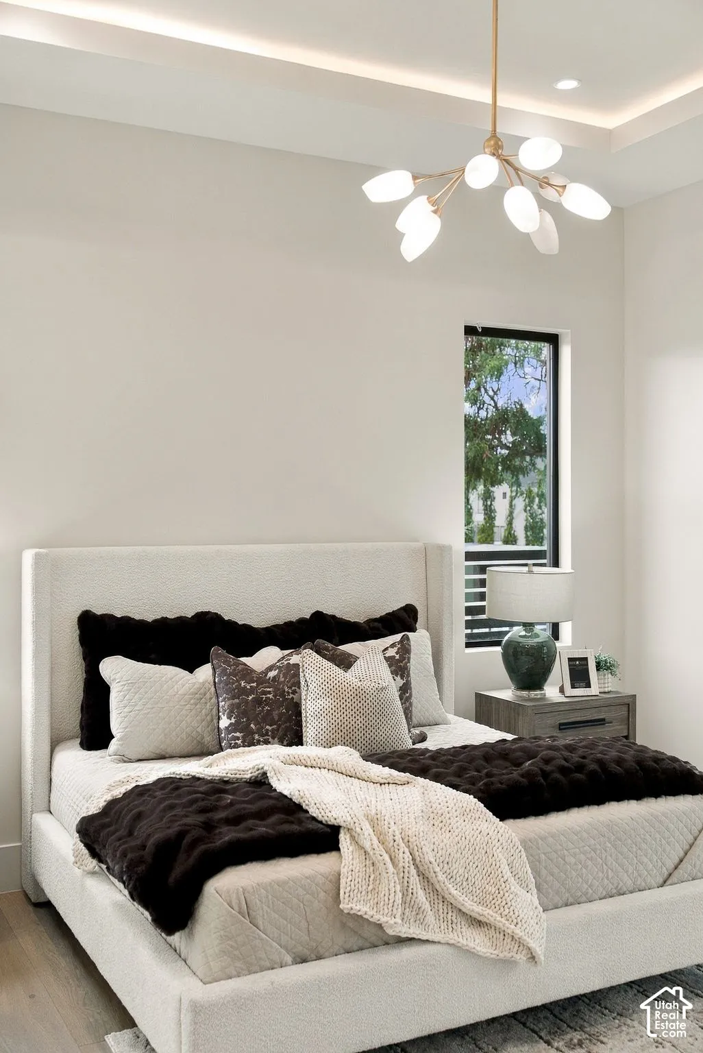 Tray ceiling featuring recessed lighting and a multi-arm metallic chandelier with frosted glass shades, complemented by a tall, slim window with a black frame