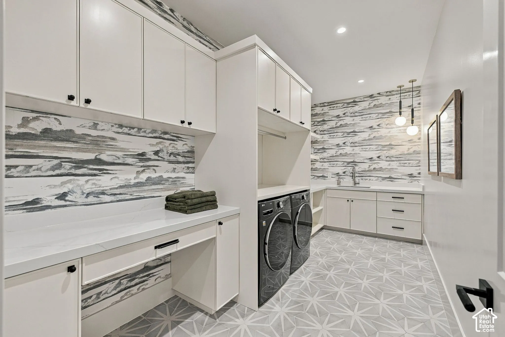 Laundry room featuring custom white cabinetry, stone-finish countertops, geometric-patterned tile flooring, a stainless steel undermount sink with a gooseneck faucet, and dual pendant lighting