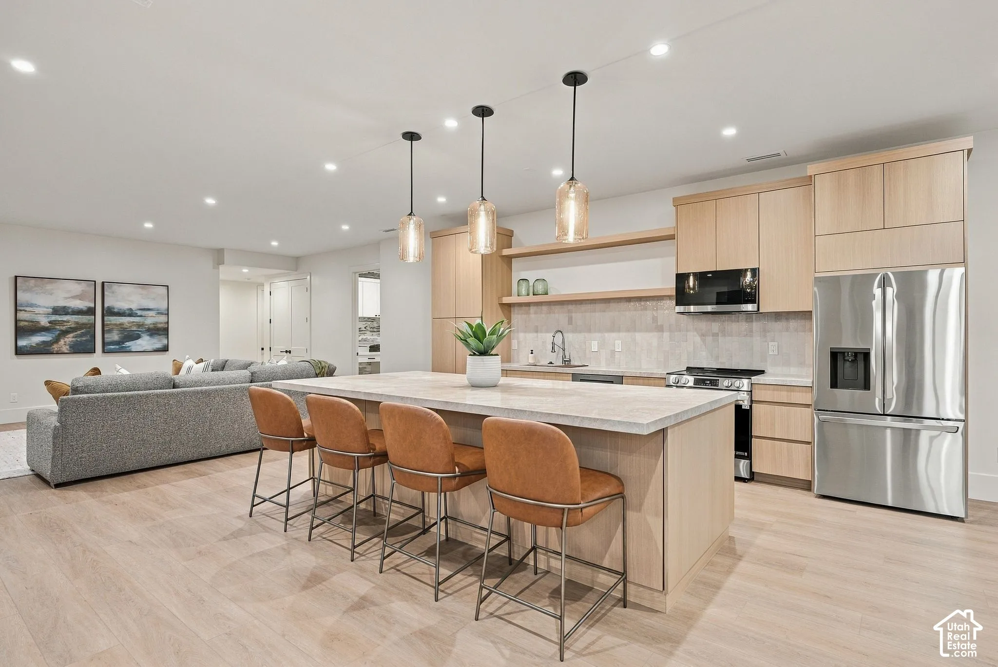Kitchen featuring light wood-finish cabinetry, a central island with stone-finish countertops, recessed lighting, glass pendant fixtures, and stainless-steel appliances