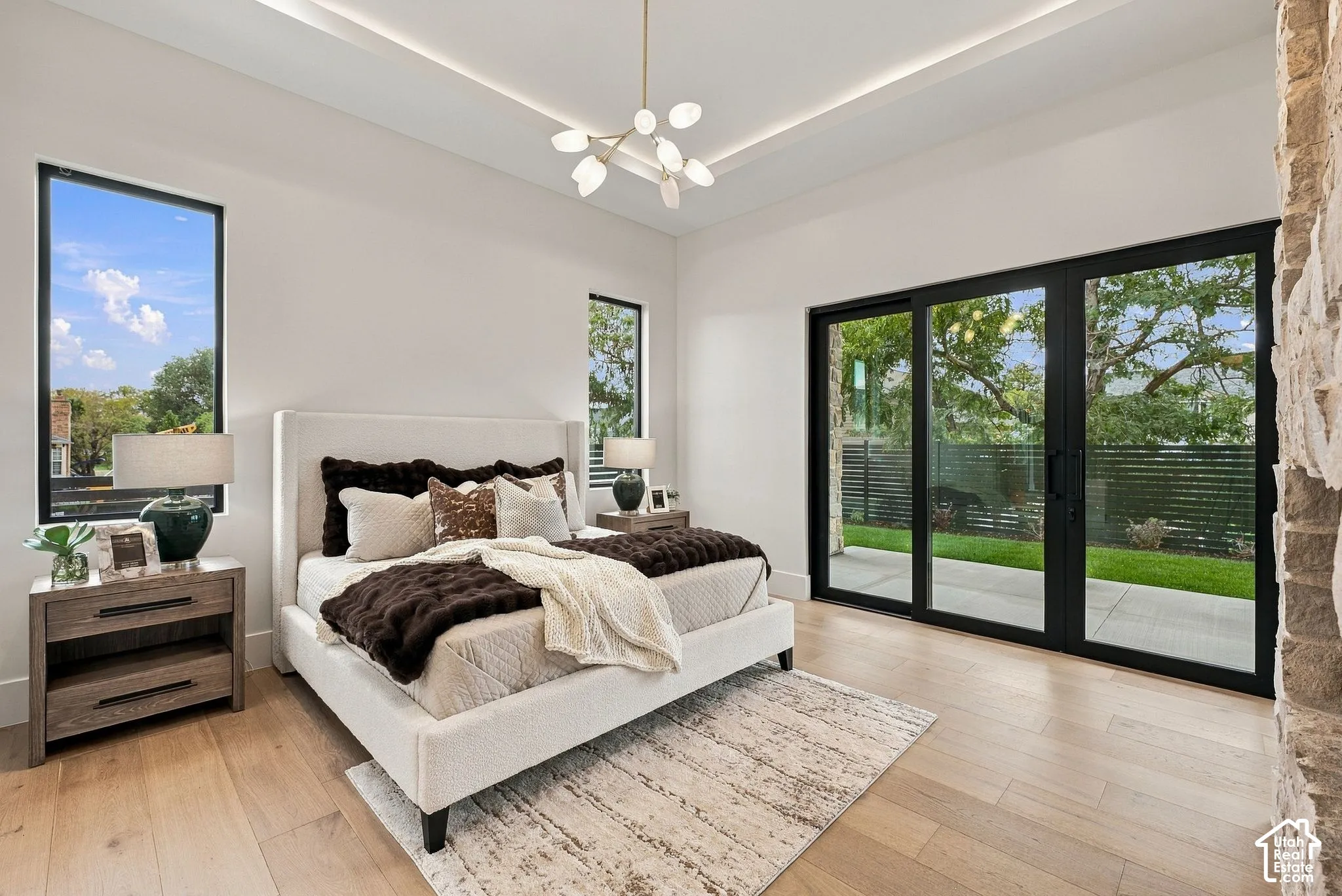 Tray ceiling with recessed lighting, wood-finish flooring, multi-pane sliding glass doors, and a natural stone feature wall