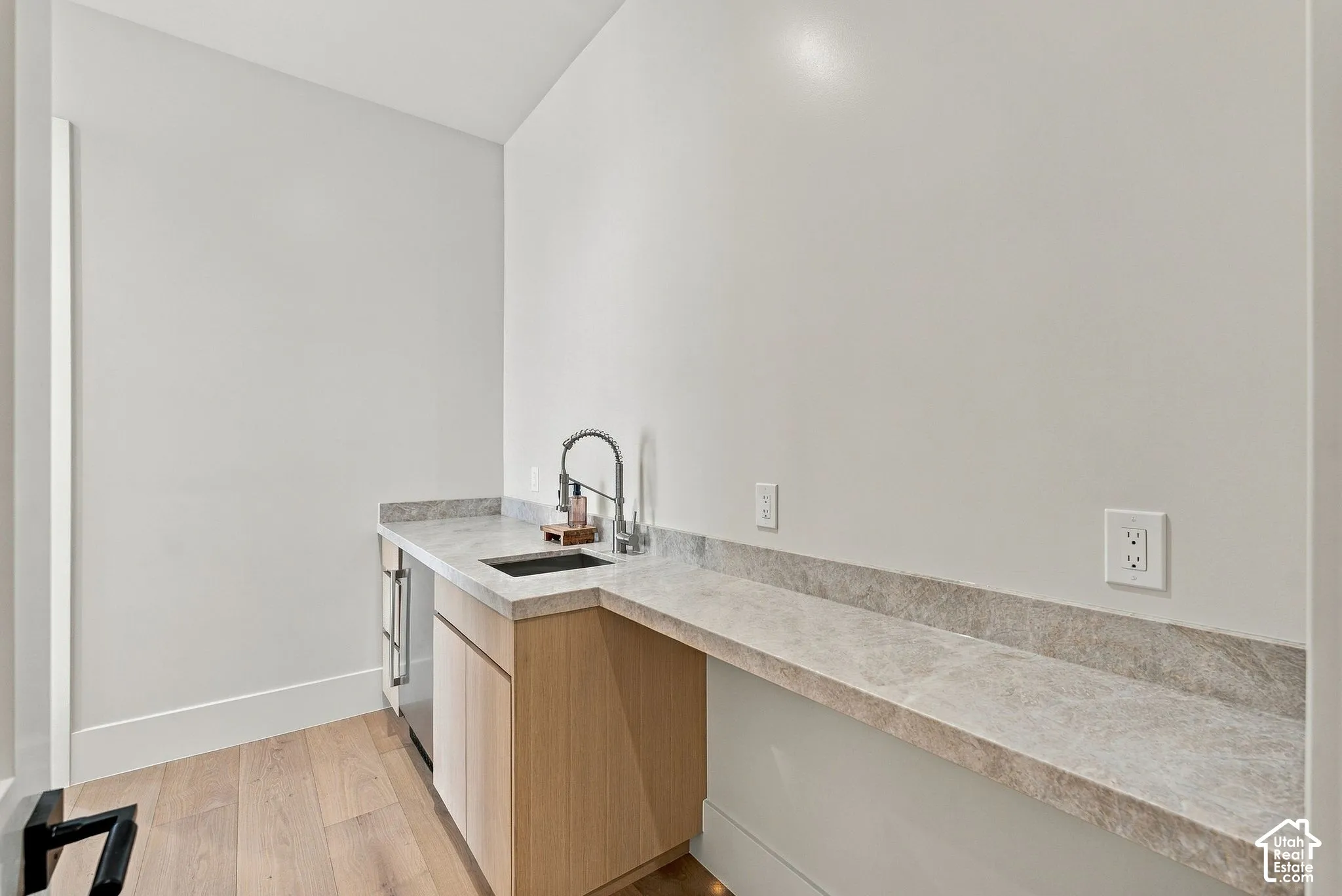 Built-in wet bar featuring light wood cabinetry, stone-finish countertops, an undermount sink with a gooseneck faucet, and wood-finish flooring