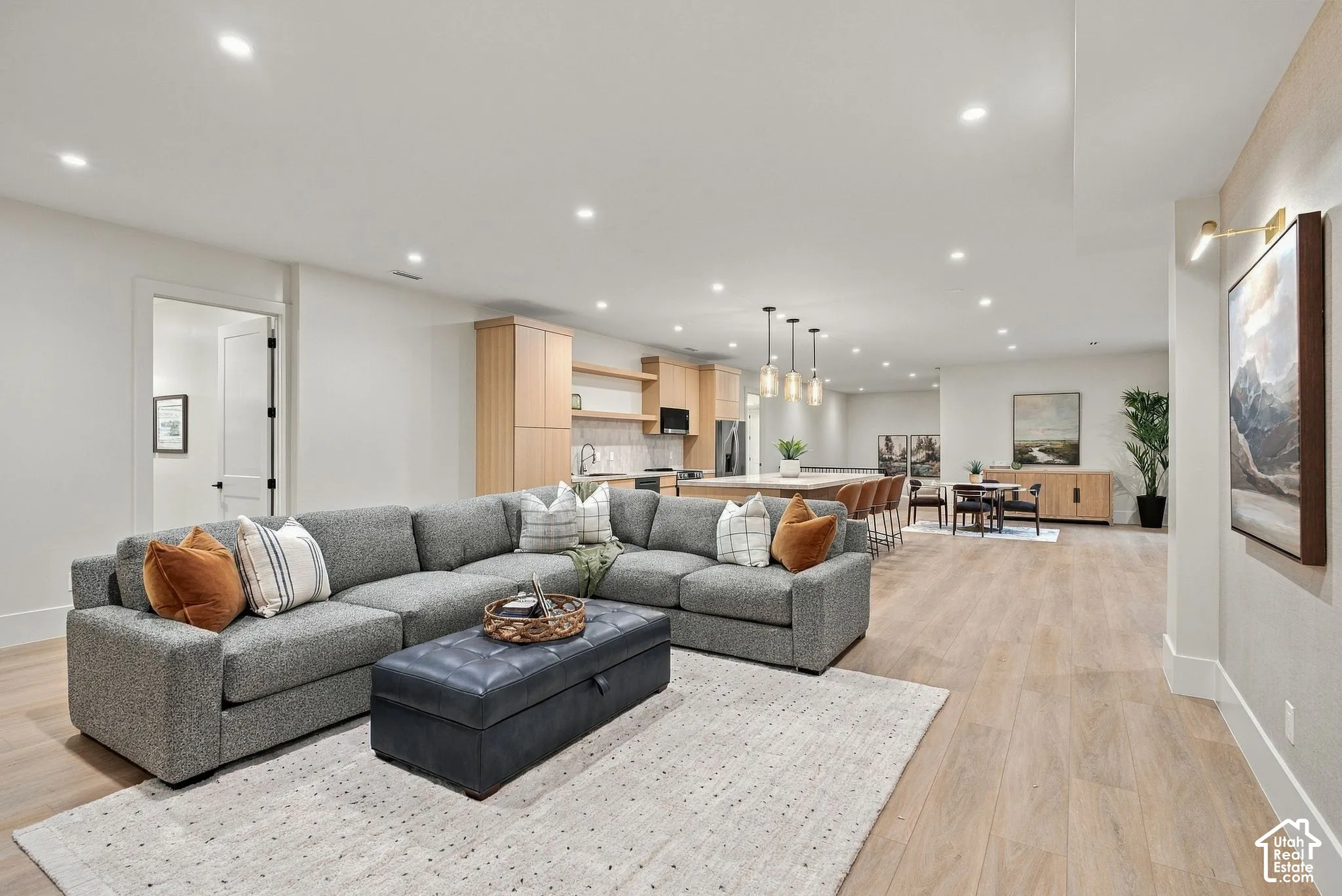 Open-concept interior featuring light wood-finish flooring, recessed lighting, neutral wall palette, custom light wood cabinetry, and a central kitchen island