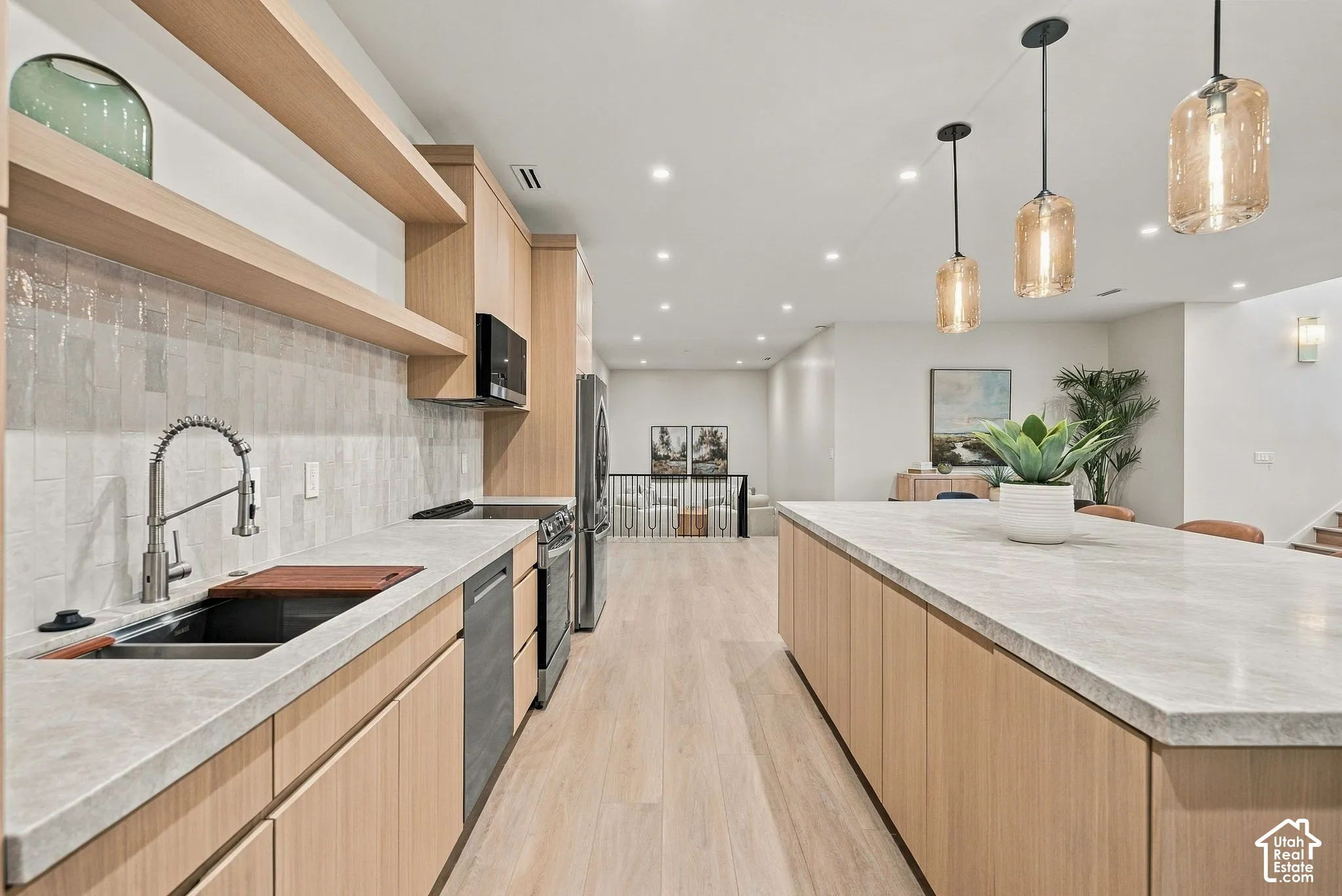 Kitchen featuring light wood-finish cabinetry, stone countertops, textured tile backsplash, wood-finish flooring, and pendant lighting
