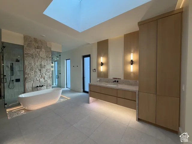 Spacious bath featuring a freestanding soaking tub with recessed perimeter lighting, a large skylight, and a stone accent wall