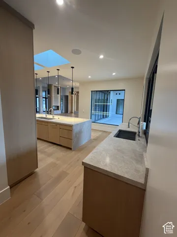 Open-concept kitchen featuring light wood-finish cabinetry, stone countertops, and wide plank wood-finish flooring