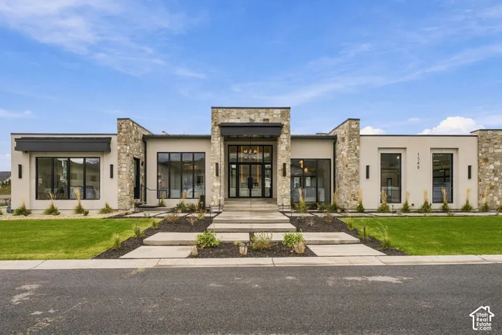 Luxury Contemporary exterior featuring a combination of natural stone and smooth stucco siding, prominent floor-to-ceiling windows with black metal frames, a covered glass-paneled double door entrance, and structured concrete hardscaping