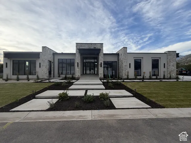 Modern architectural facade featuring stone accents, large black-framed windows, a flat roofline, and a stunning 12 ft glass front entrance