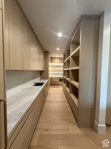 Modern galley-style pantry featuring extensive custom wood cabinetry, light-toned wood-finish flooring, integrated countertop cooktop, stone countertops, and recessed lighting