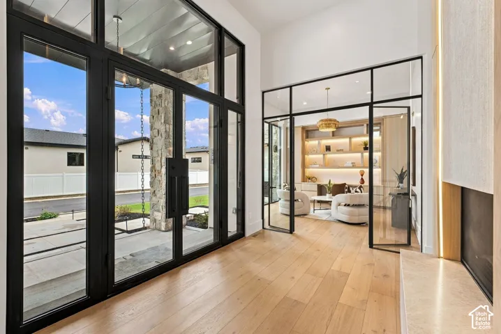 Expansive foyer featuring floor-to-ceiling black-framed glass entry doors, wood-finish flooring, and a stone-clad fireplace hearth