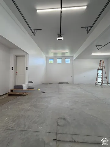 Spacious garage featuring a concrete floor, multiple fluorescent light fixtures, a white painted ceiling, and three square windows providing natural light