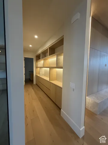 Hallway to the guest suite featuring wood-finish flooring, built-in shelving with integrated lighting, built-in cabinetry with drawers, recessed ceiling lighting