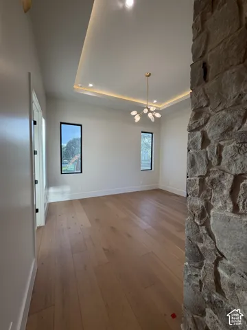 Spacious Primary bedroom featuring wood-finish flooring, a tray ceiling with recessed lighting and cove lighting, a contemporary chandelier double sided fireplace and sliding glass door